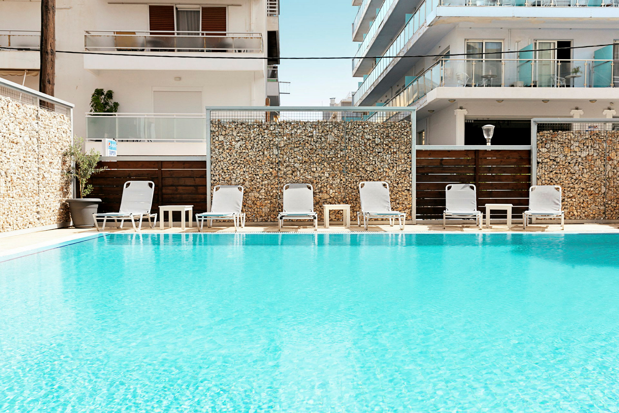 Swimmingpool med liggestole og borde foran bygninger. (AI-genereret tekst)