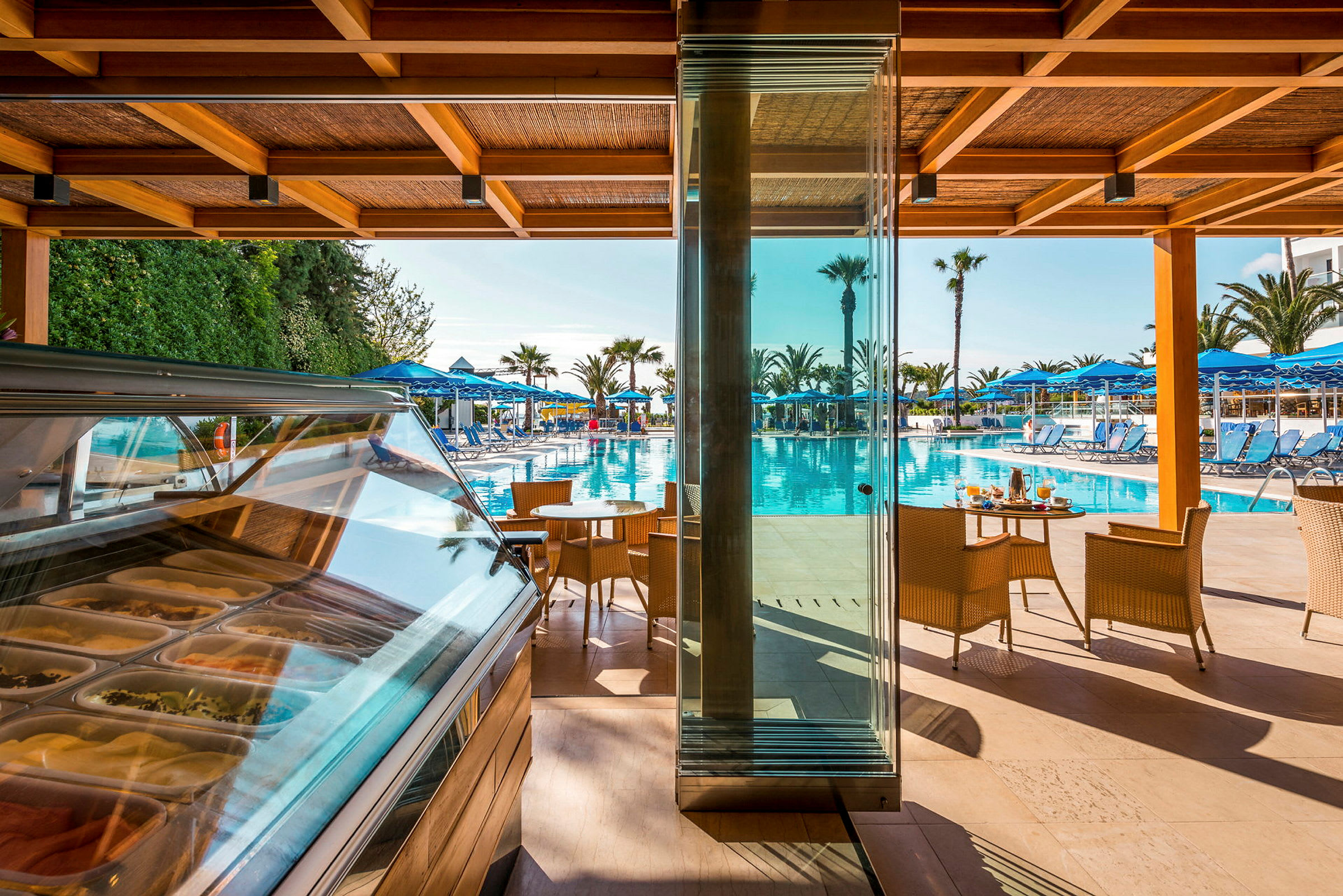Udsigt over en pool med liggestole og parasoller set fra en terrasse med glasvægge og siddepladser. (AI-genereret tekst)