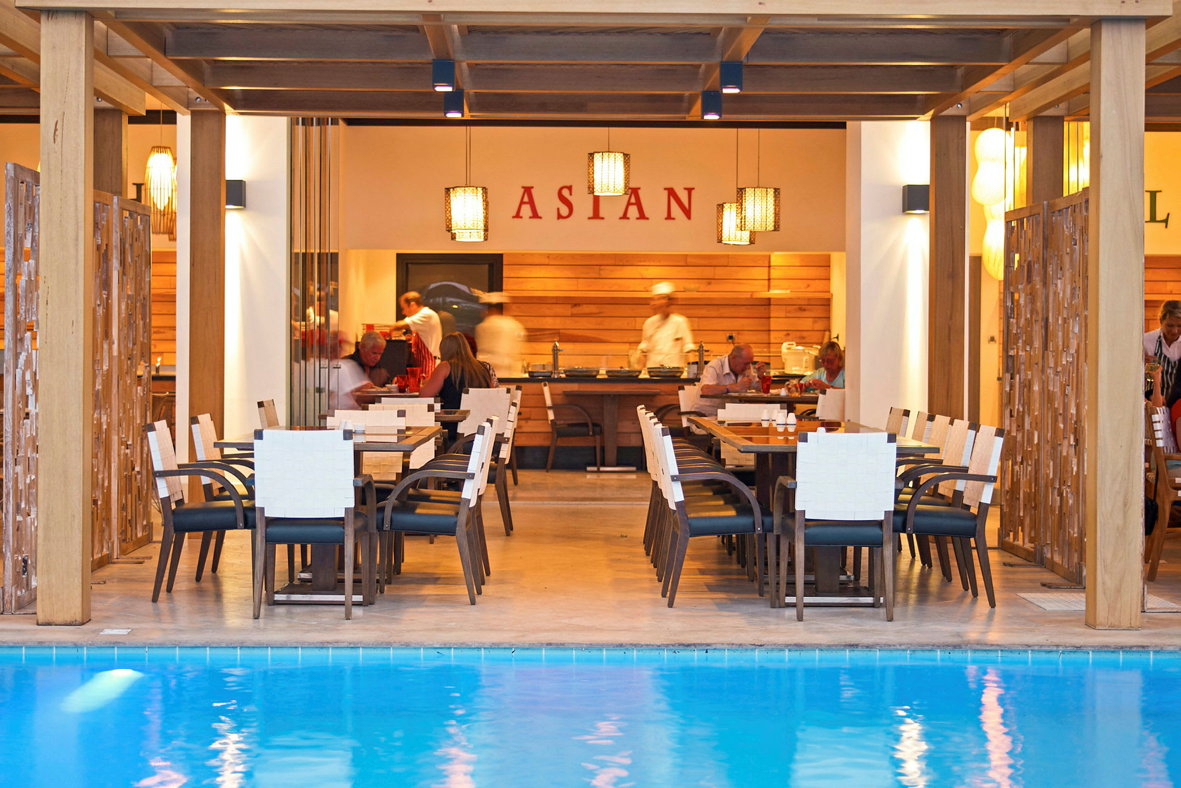 Restaurant ved en pool med borde og stole foran en serveringsområde. (AI-genereret tekst)