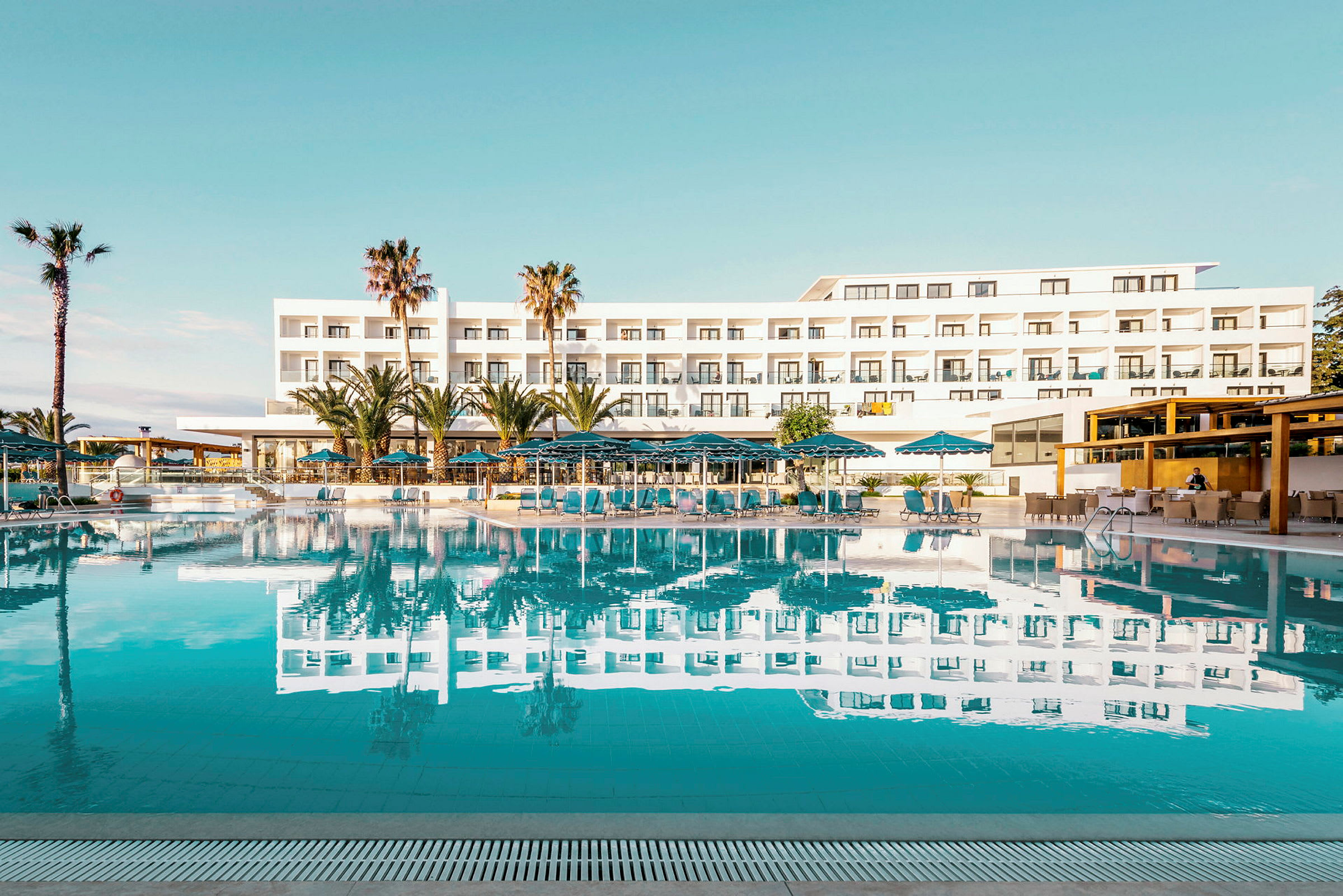 Hotelbygning med pool og liggestole i forgrunden. (AI-genereret tekst)