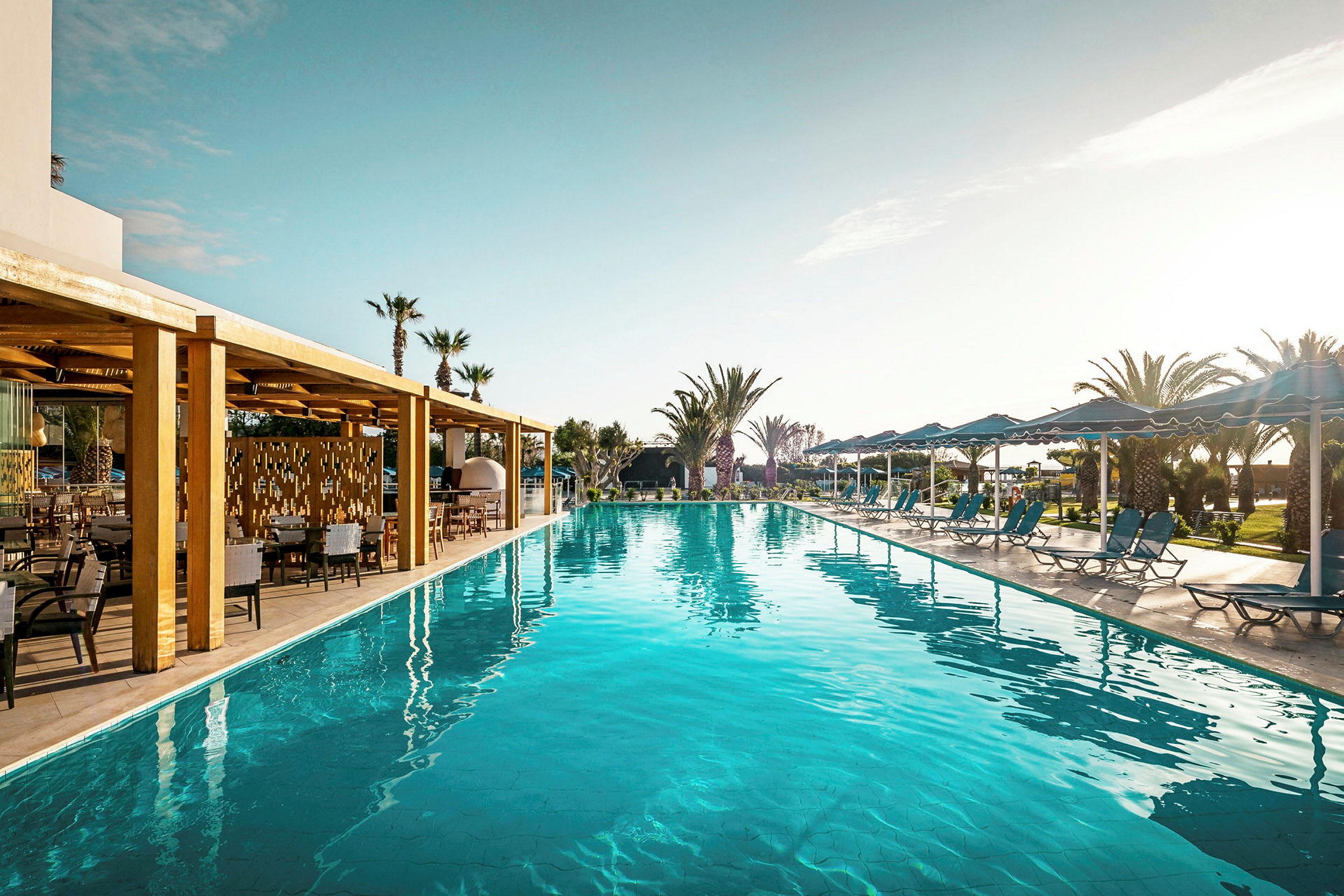 En pool med solsenge og parasoller samt en træbeklædt terrasse ved siden af. (AI-genereret tekst)