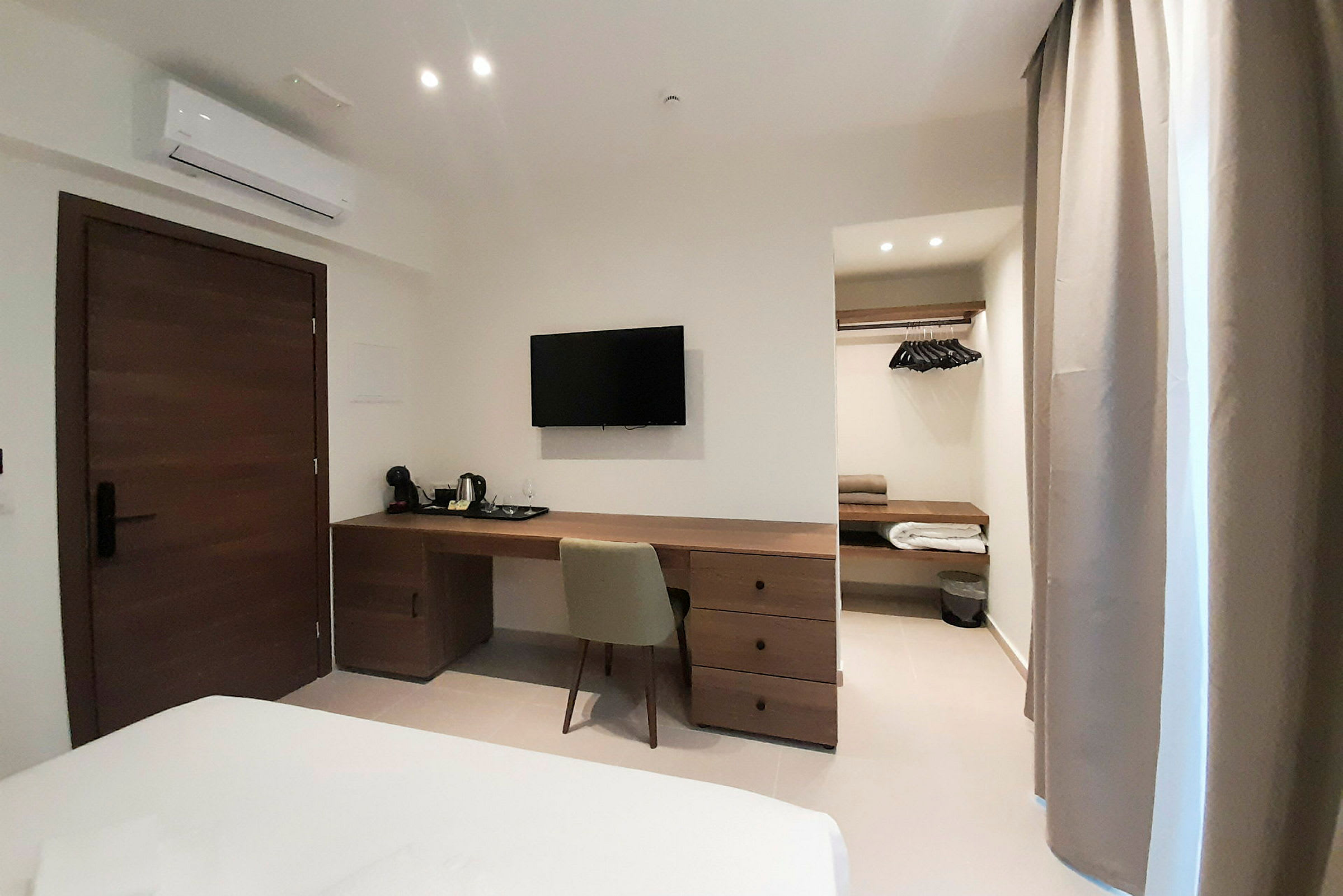 Hotelværelse med skrivebord, stol, tv, garderobe og aircondition. (AI-genereret tekst)