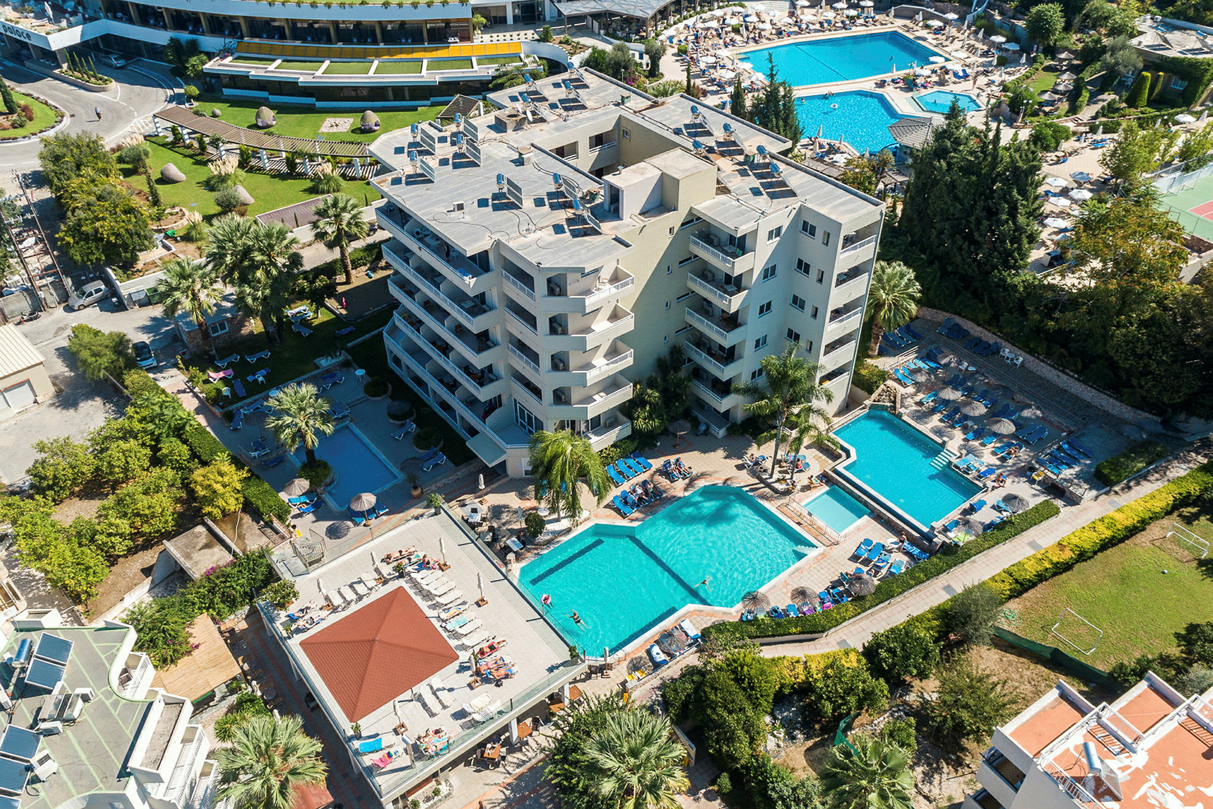 Luftfoto af hotel med poolområder, liggestole og grønne omgivelser. (AI-genereret tekst)