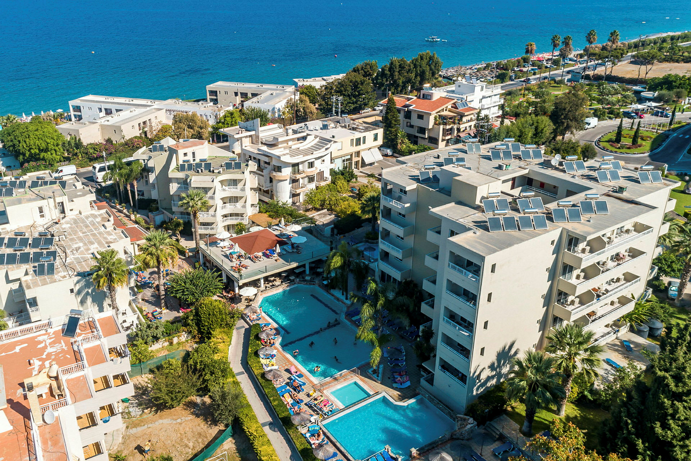 Luftfoto af hotelområde med bygninger, swimmingpools og omliggende grønne områder ved havet. (AI-genereret tekst)