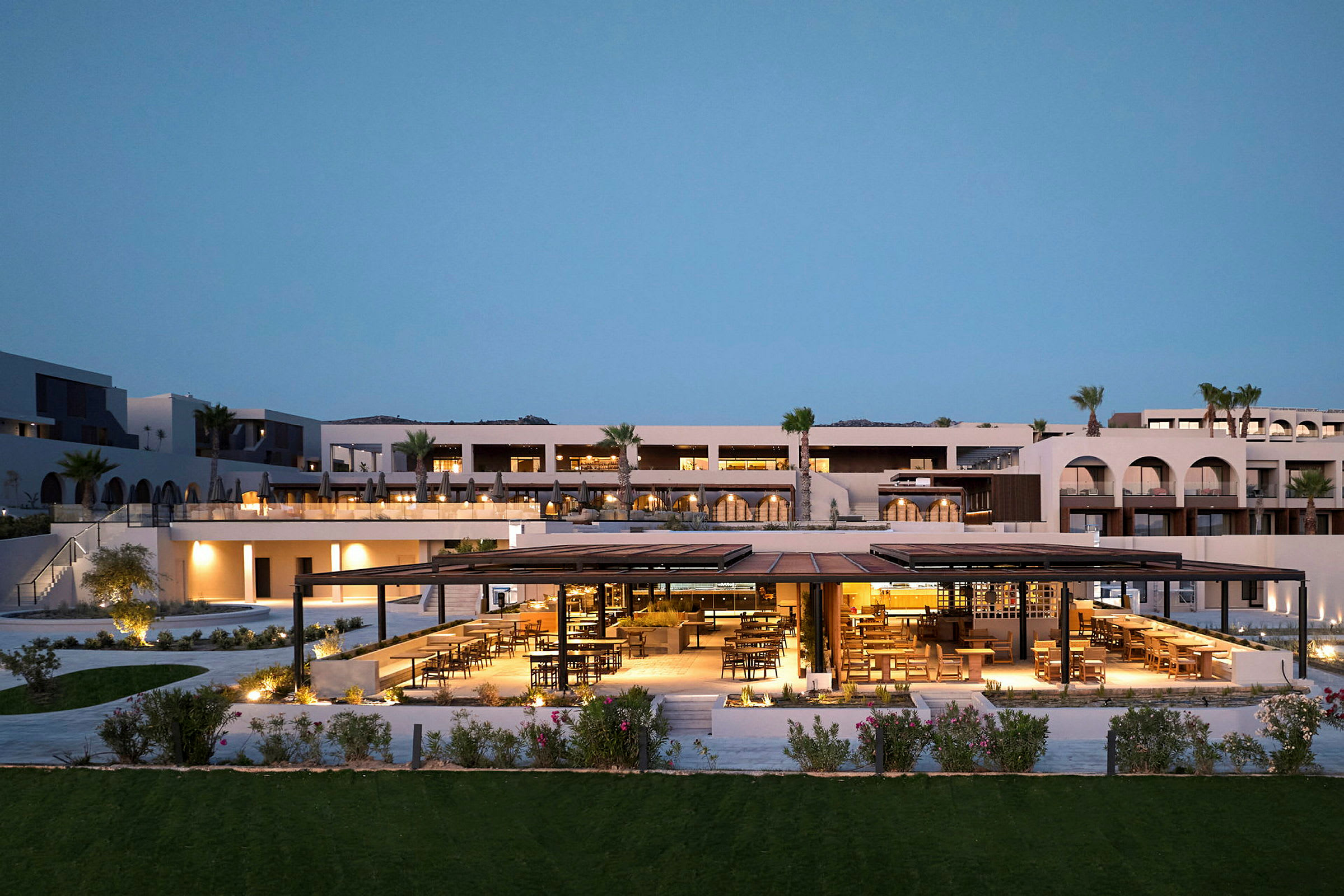 Luksusresort i moderne stil med oplyst udendørsrestaurant og aftensbelysning. (AI-genereret tekst)