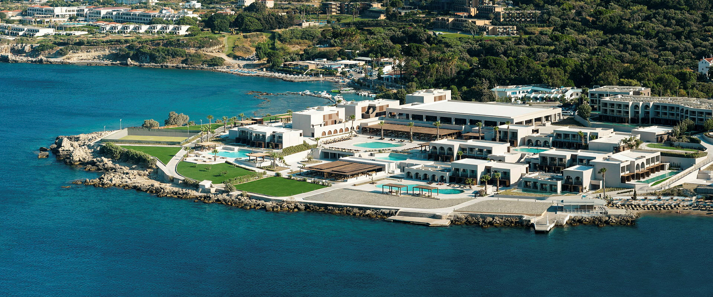Luftfoto af et hotelkompleks ved kysten med pools og grønne områder. (AI-genereret tekst)