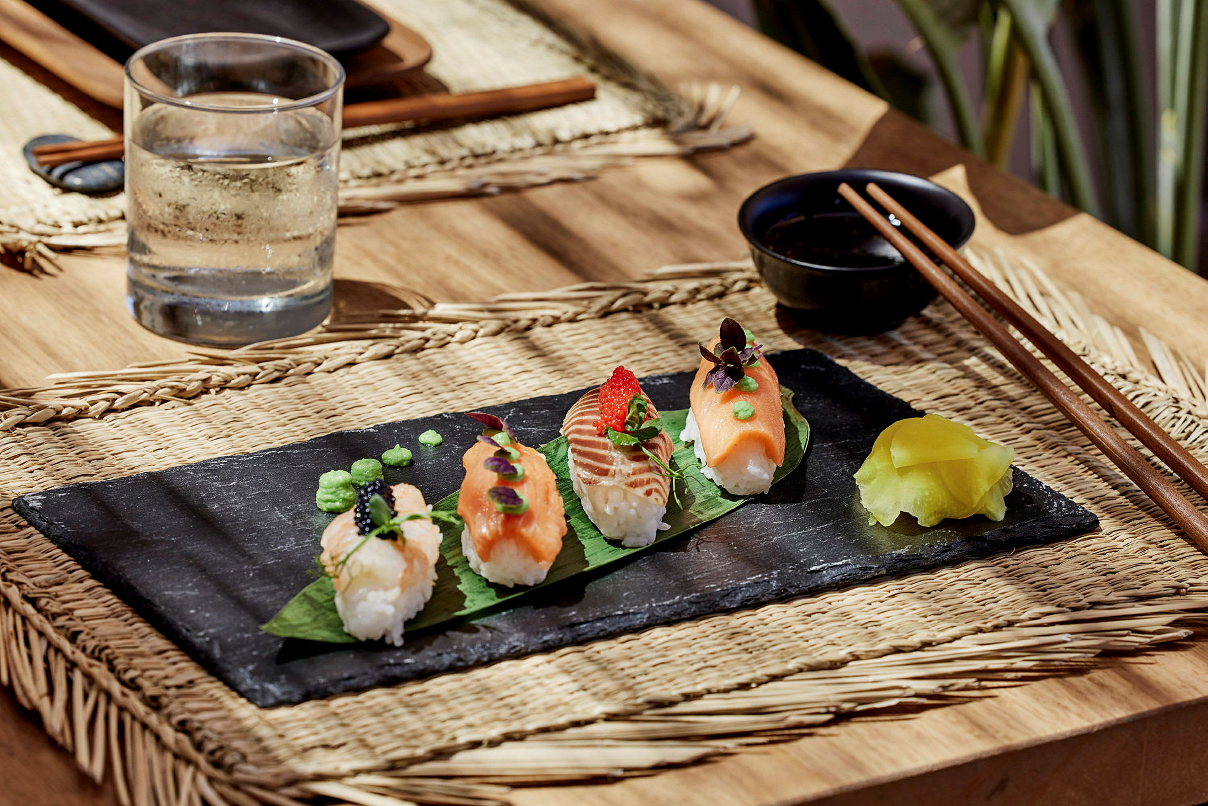 Sushi stykker på en sort platte med en vandkande og spisepinde ved siden af. (AI-genereret tekst)