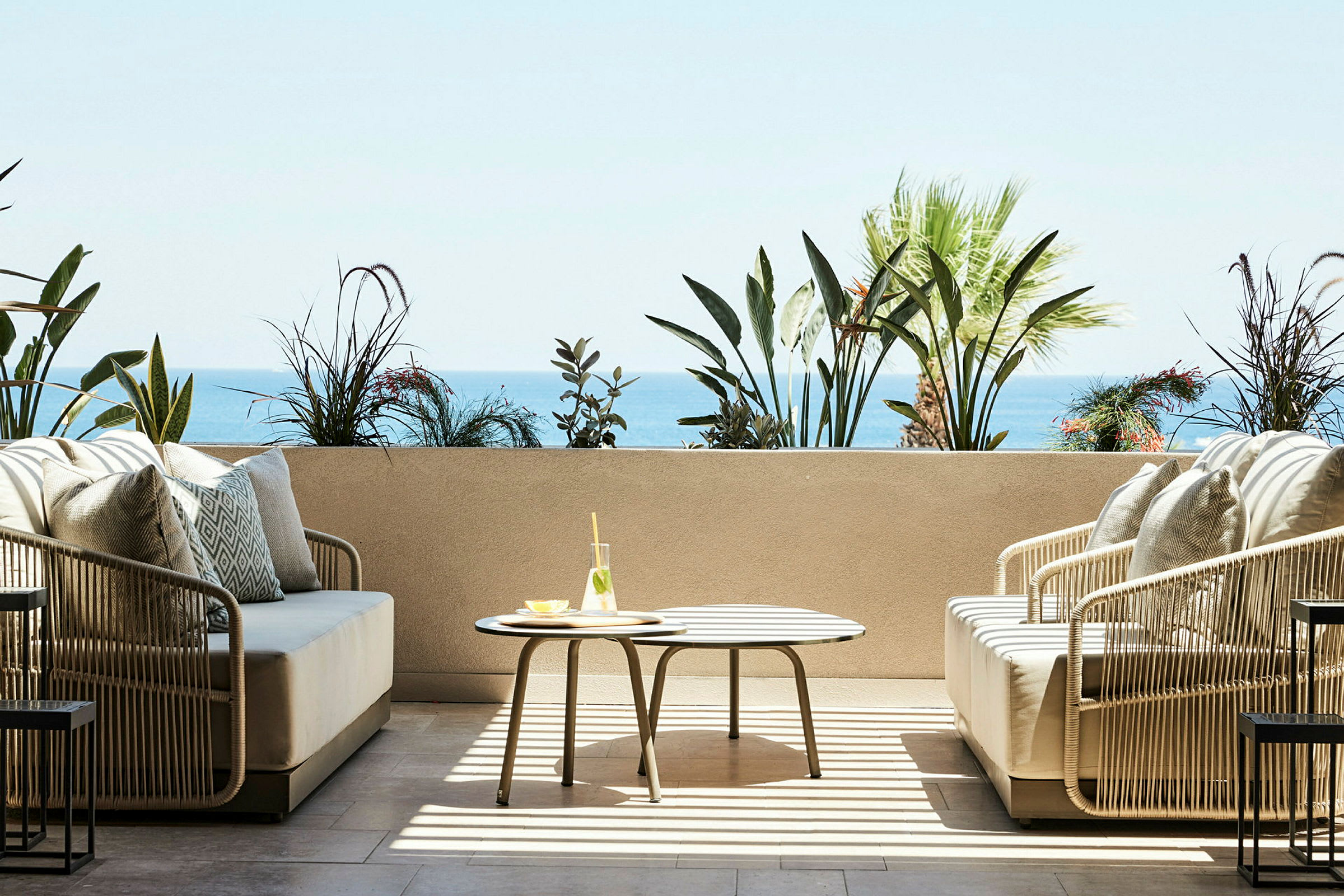 Terrasse med siddepladser, bord med glas og havudsigt i baggrunden. (AI-genereret tekst)