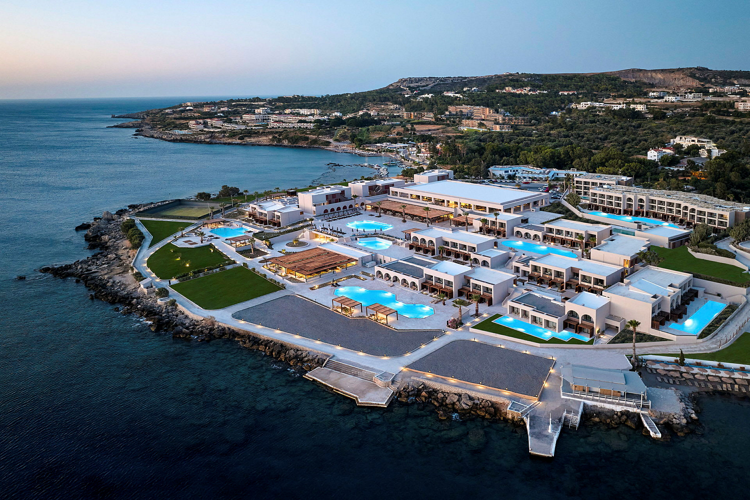 Luftfoto af en resort ved havet med mange bygninger og swimmingpools. (AI-genereret tekst)
