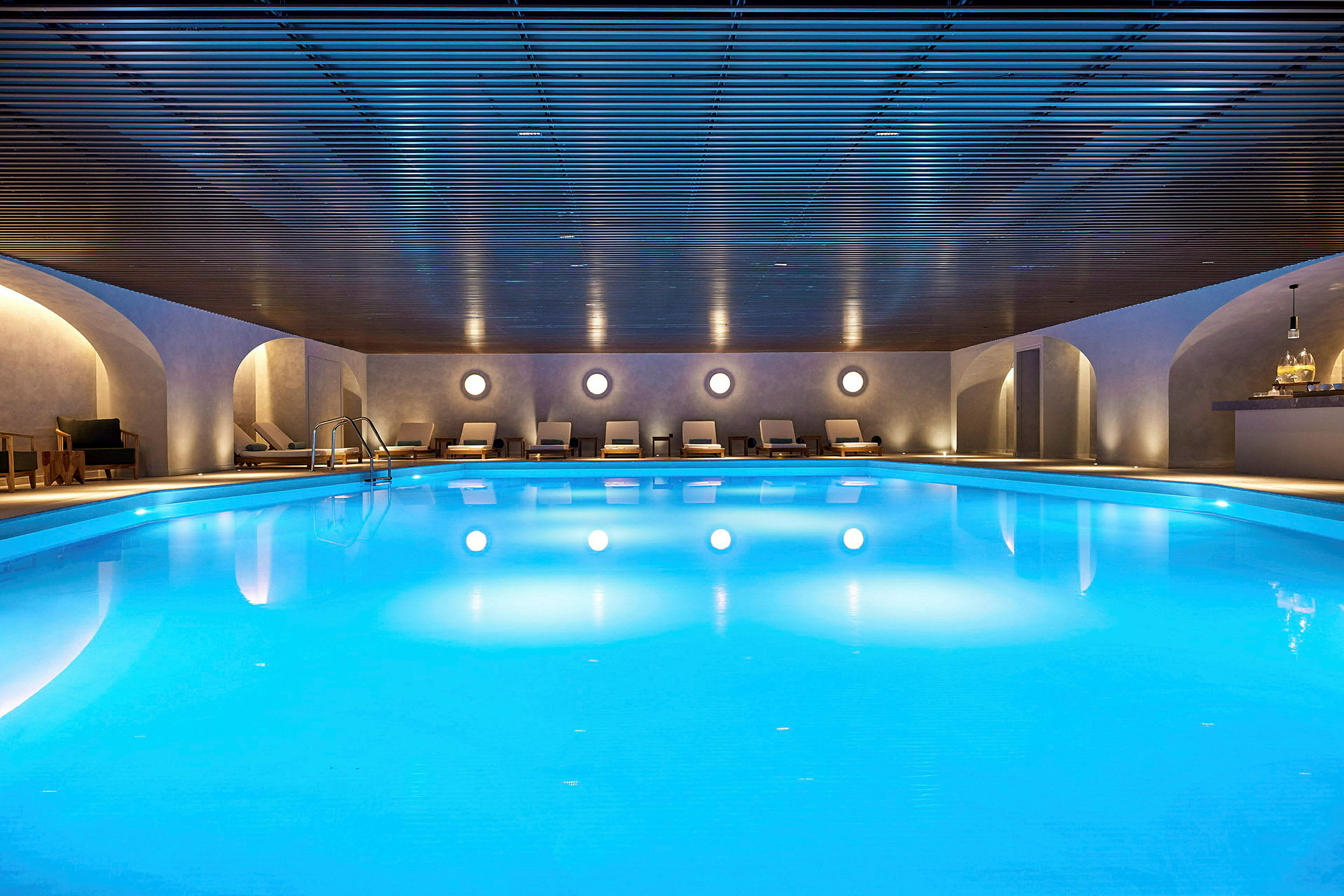 Indendørs pool med blåt vand og siddepladser rundt omkring. (AI-genereret tekst)