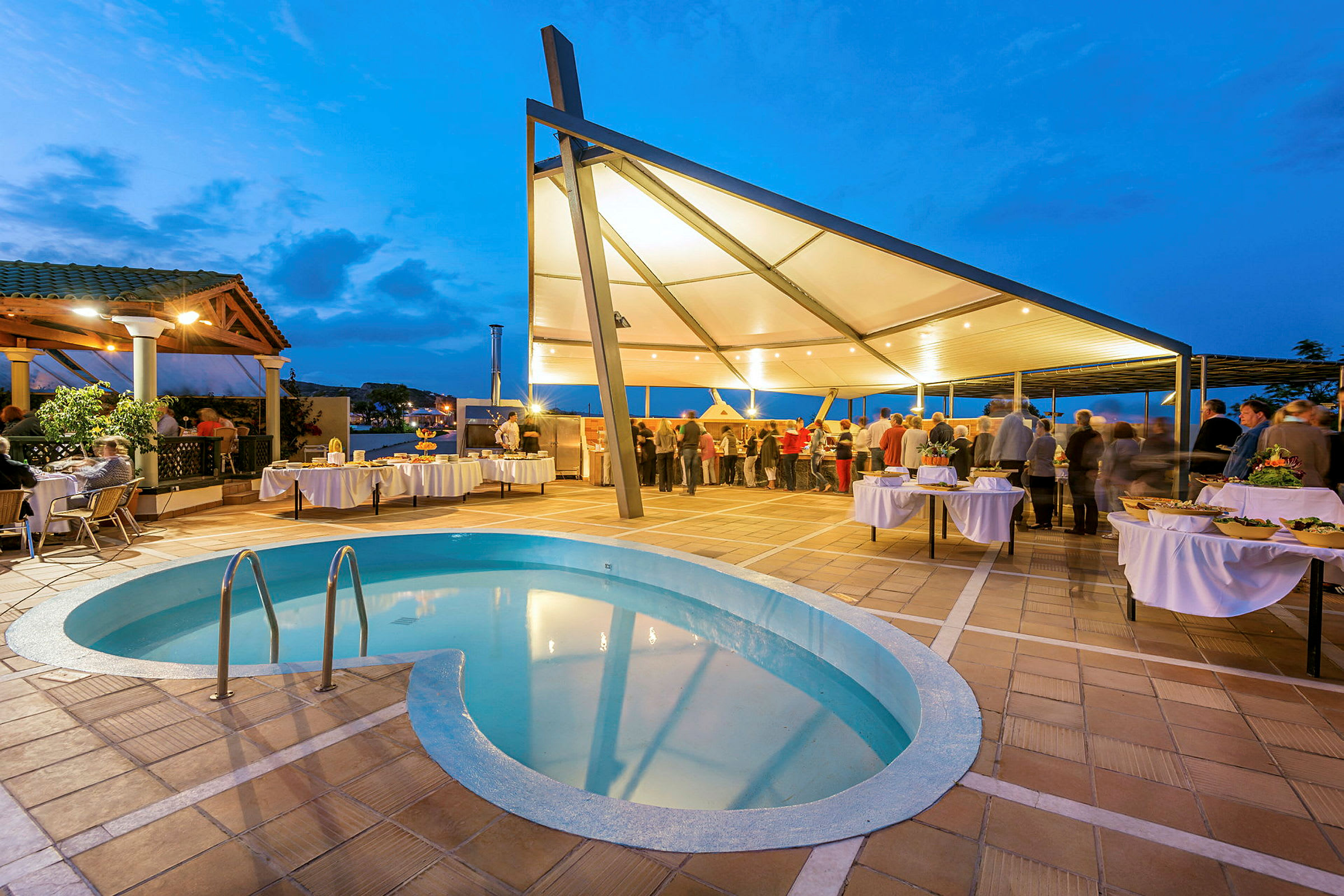 Udendørsområde med swimmingpool og telt, hvor folk samles ved spiseborde. (AI-genereret tekst)