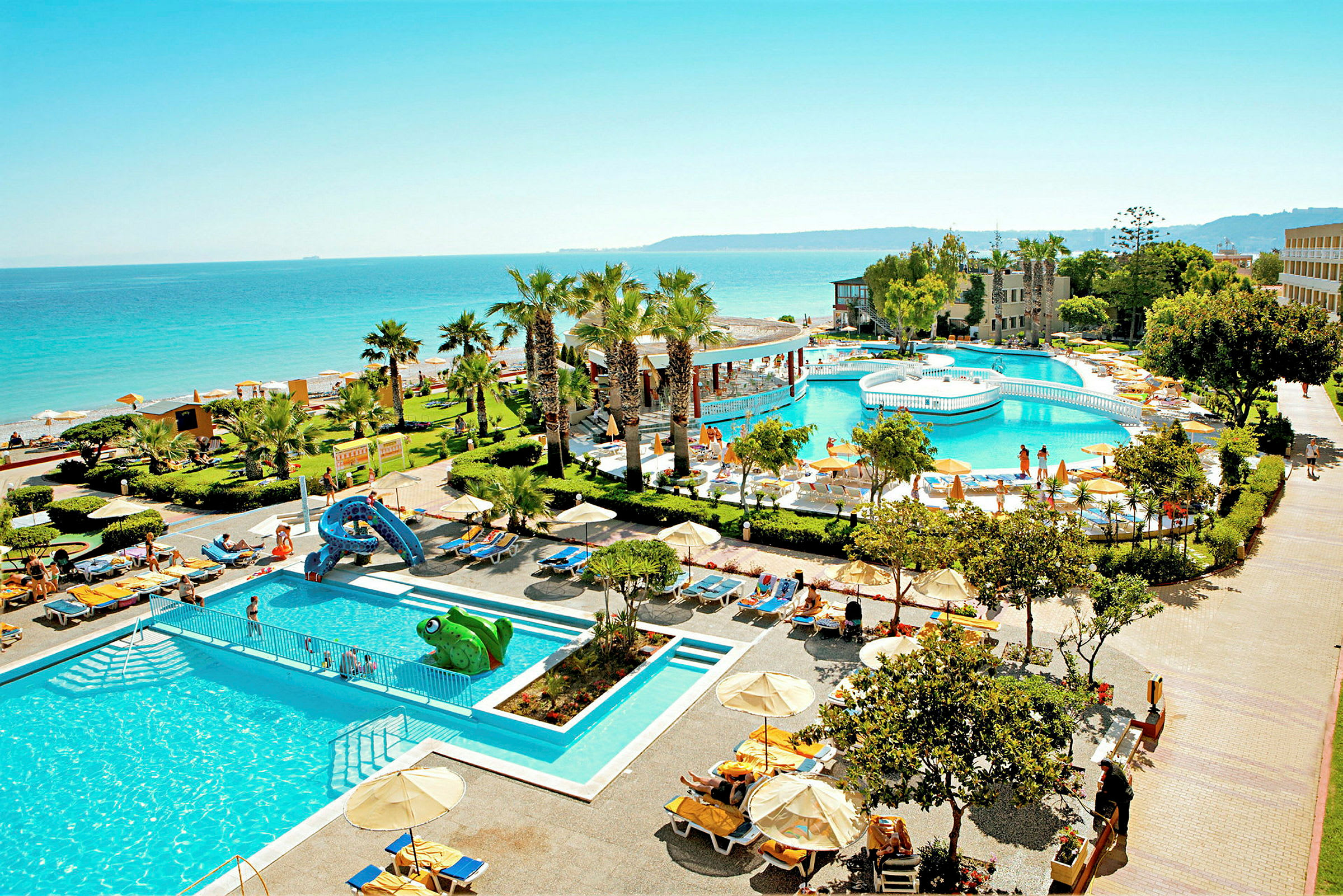 En hotelresort med poolområde og frodig have ved en strand med havudsigt. (AI-genereret tekst)