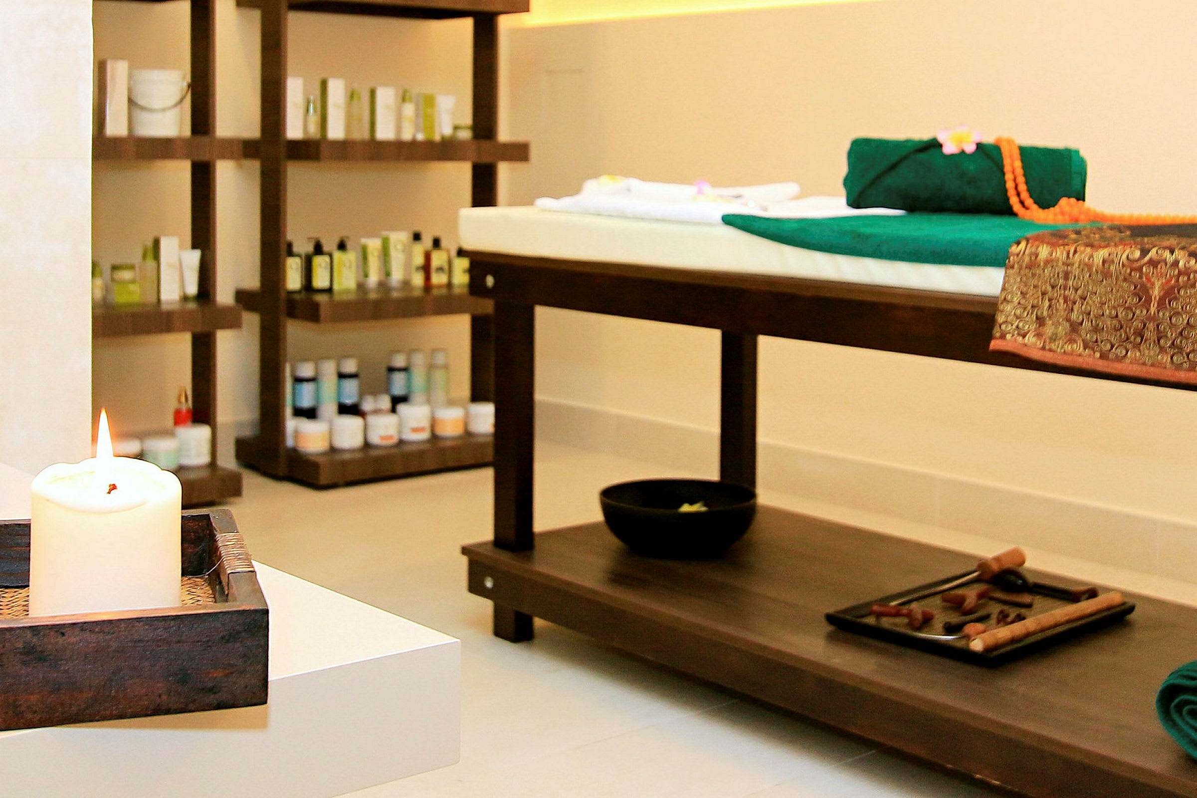 Et spa-rum med massagebriks og hylder fyldt med produkter, samt et tændt lys i forgrunden. (AI-genereret tekst)