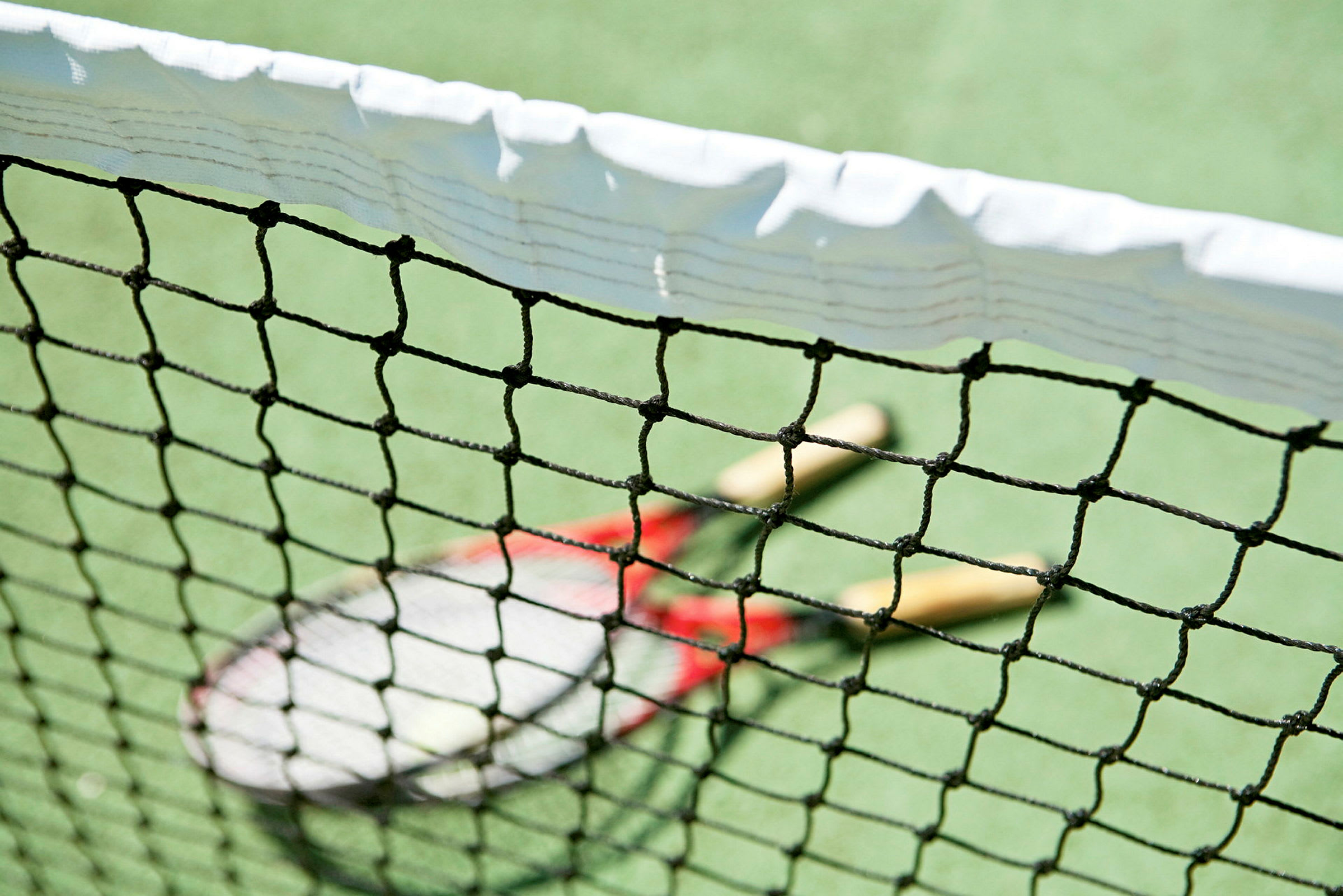 Nærbillede af et tennisnet med to tennisracketer på banen bagved. (AI-genereret tekst)