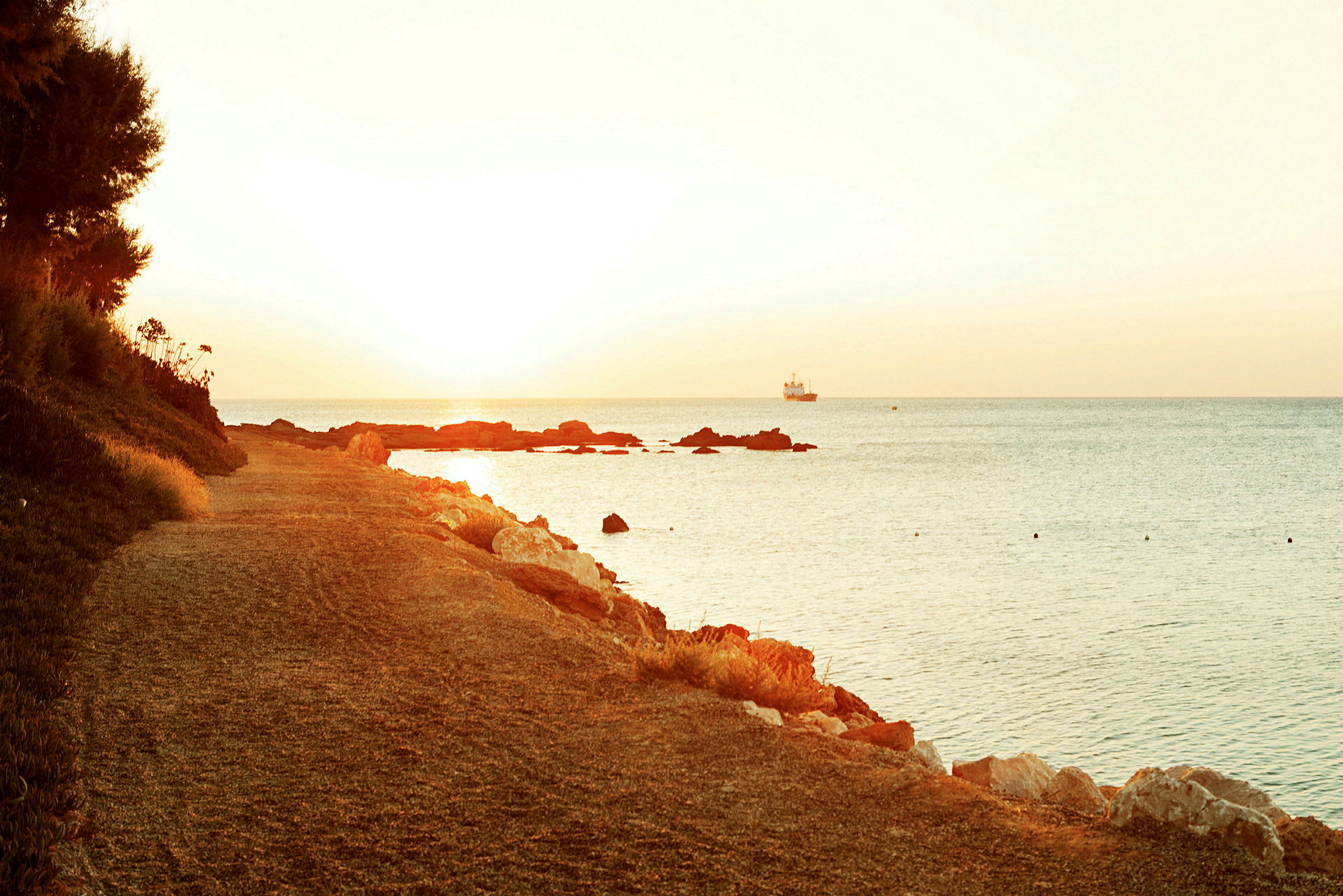 Strandpromenade ved solnedgang med havet og et skib i det fjerne. (AI-genereret tekst)