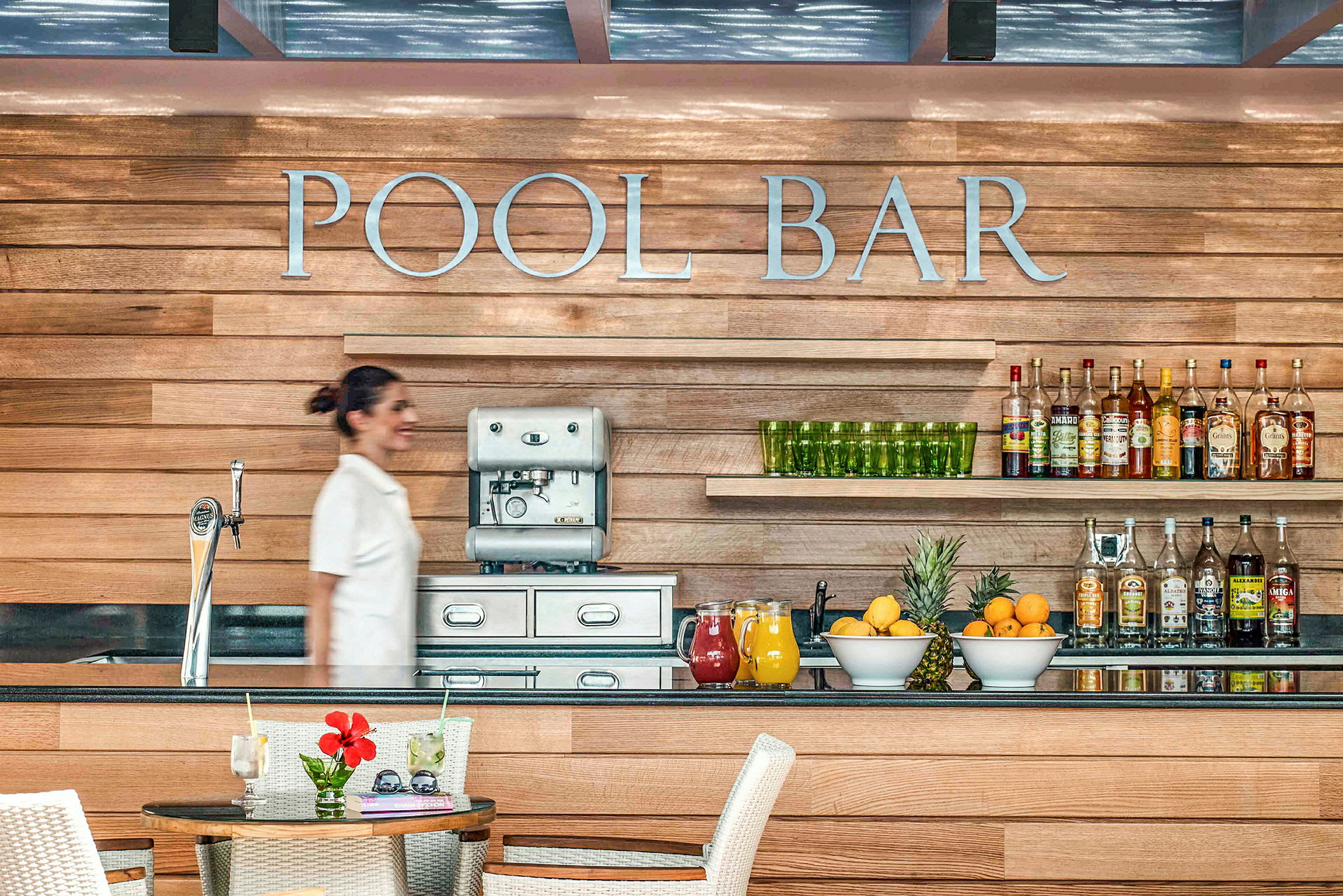 Billede af en poolbar med træpaneler, en kaffemaskine, drikkevarer og frisk frugt på disken. (AI-genereret tekst)