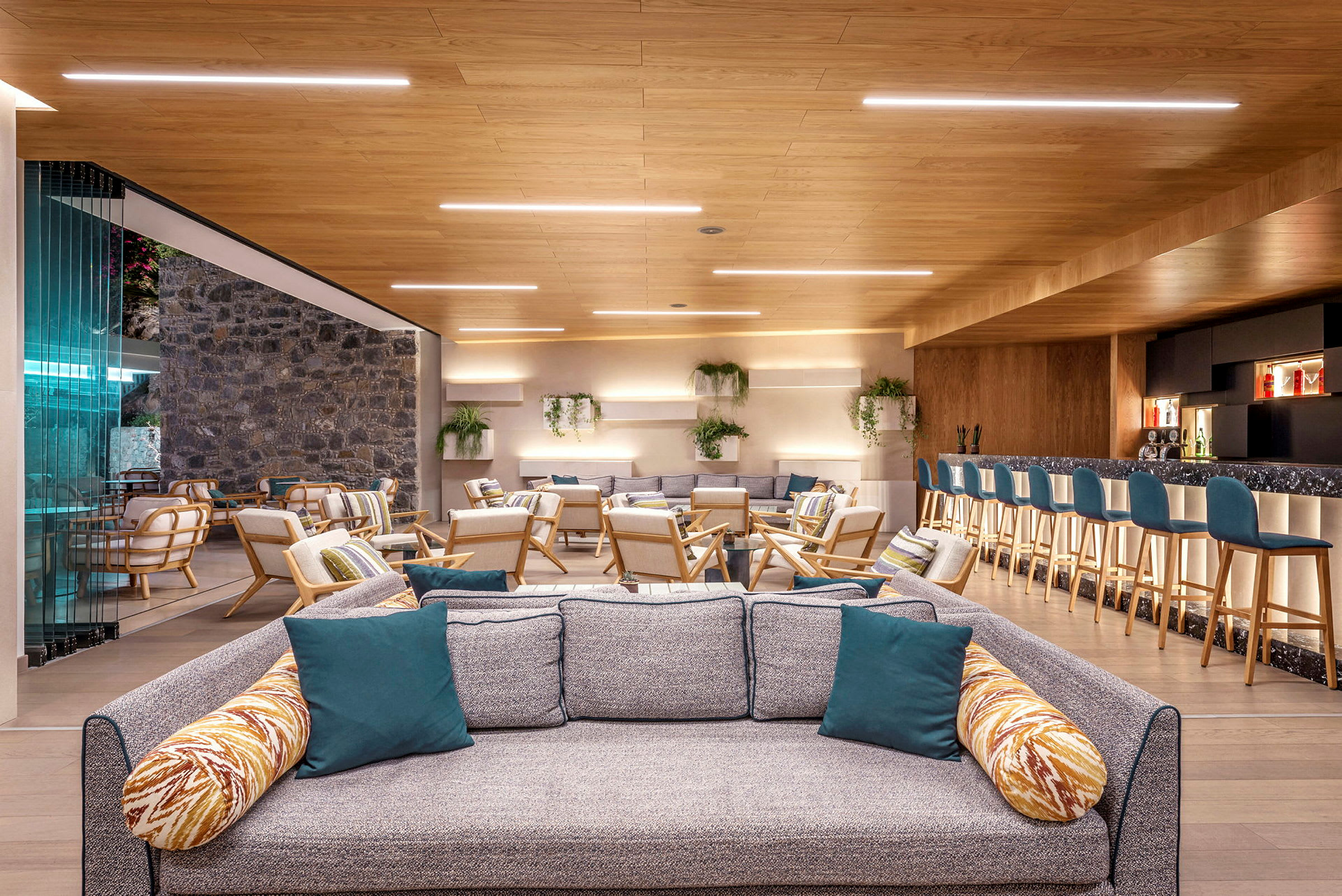 Et moderne og indbydende loungeområde med sofaer, lænestole og en bar med siddepladser. Indretningen er lys og luftig med trædetaljer og grønne planter. (AI-genereret tekst)
