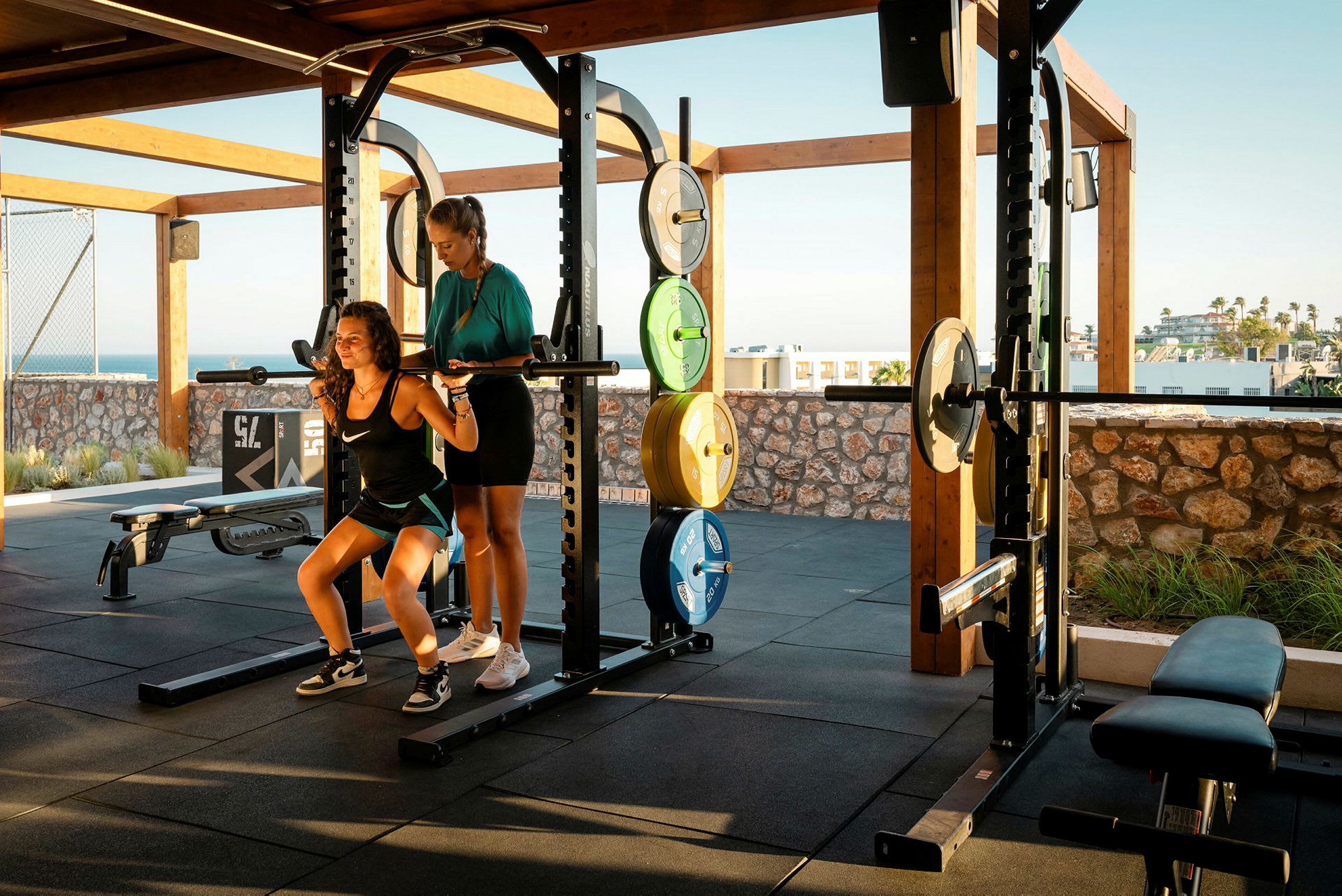 To personer træner med en vægtstang i et udendørs fitnesscenter. (AI-genereret tekst)