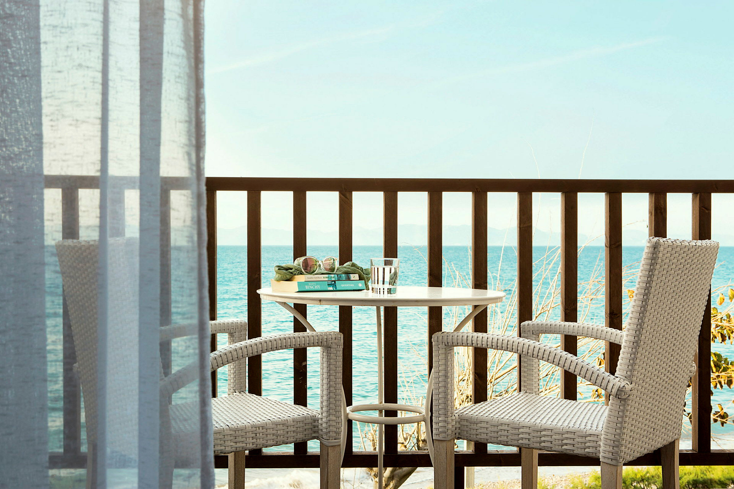To stole og et bord på en balkon med udsigt over havet. (AI-genereret tekst)