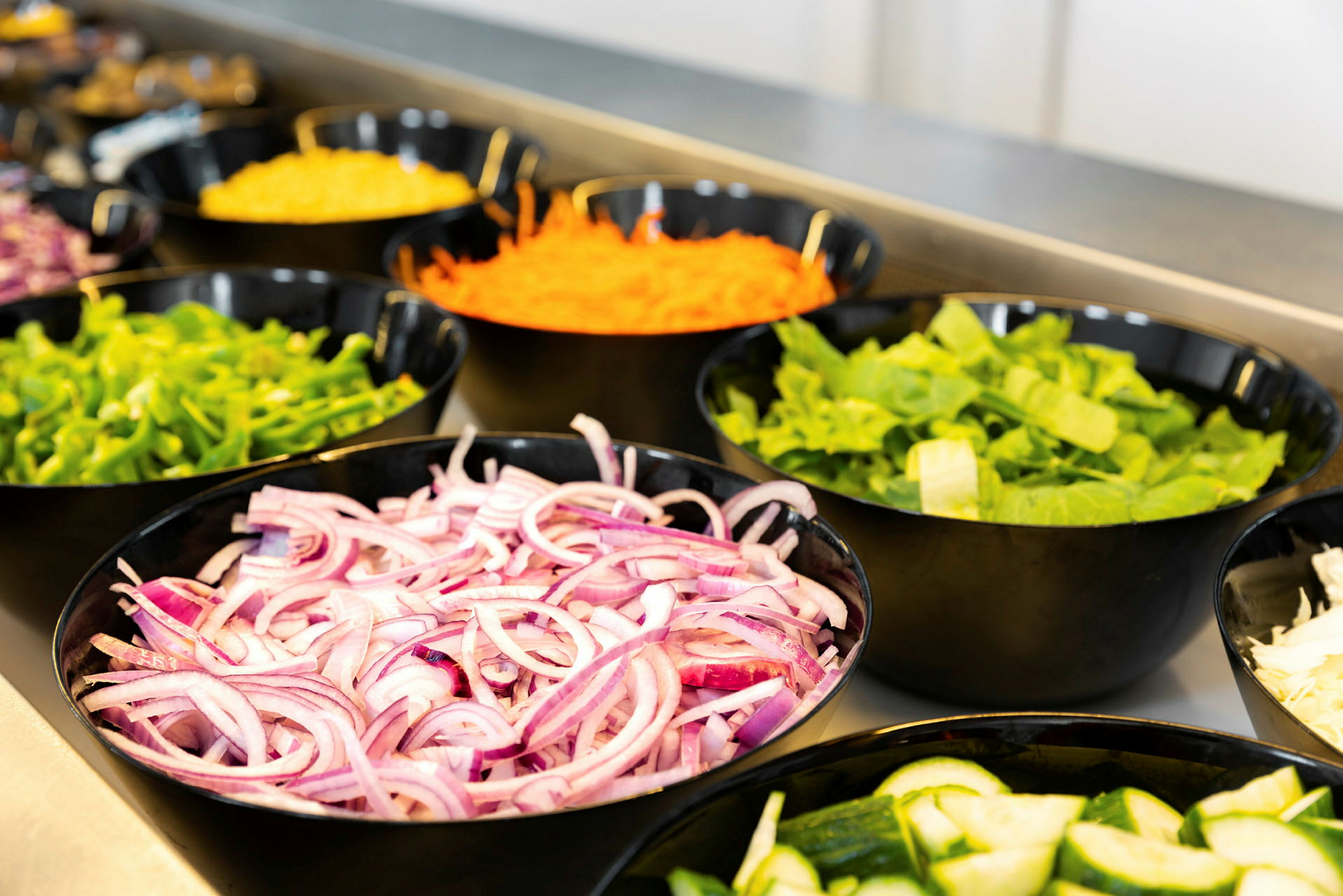 Skåle med forskellige grøntsager, herunder rødløg, agurk, salat, peberfrugt og revet gulerod. (AI-genereret tekst)