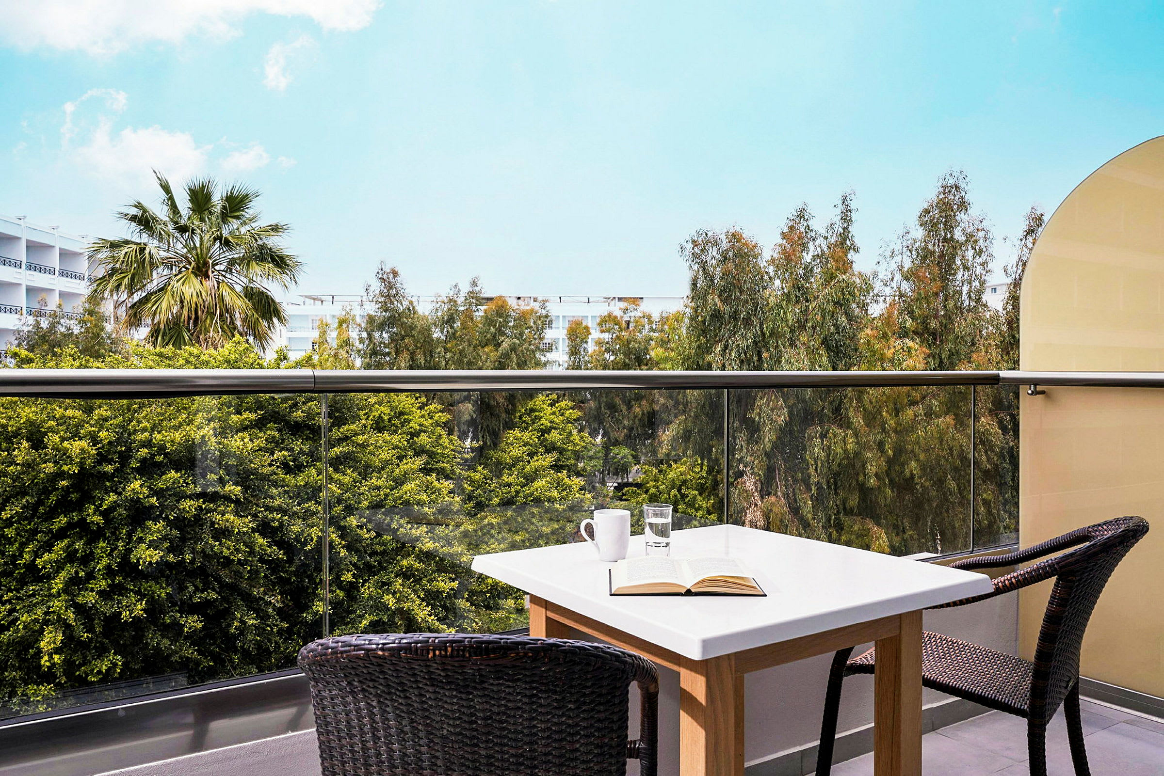 En balkon med et bord og stole, udsigt over træer og himmel. (AI-genereret tekst)