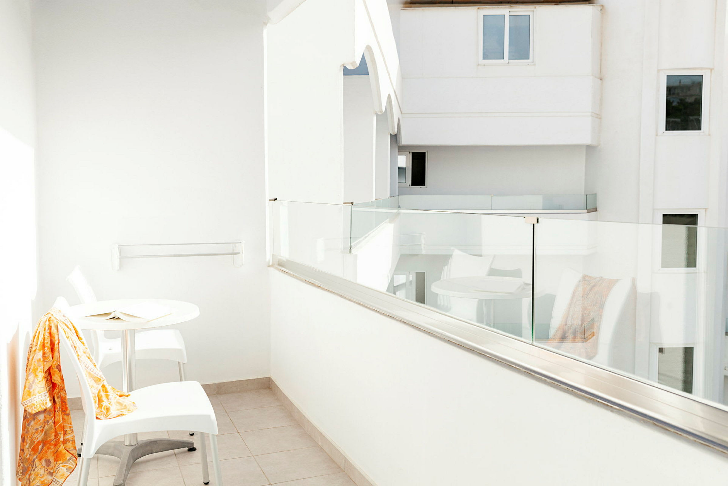 Hvid balkon med glasrækværk, et bord og to stole. (AI-genereret tekst)