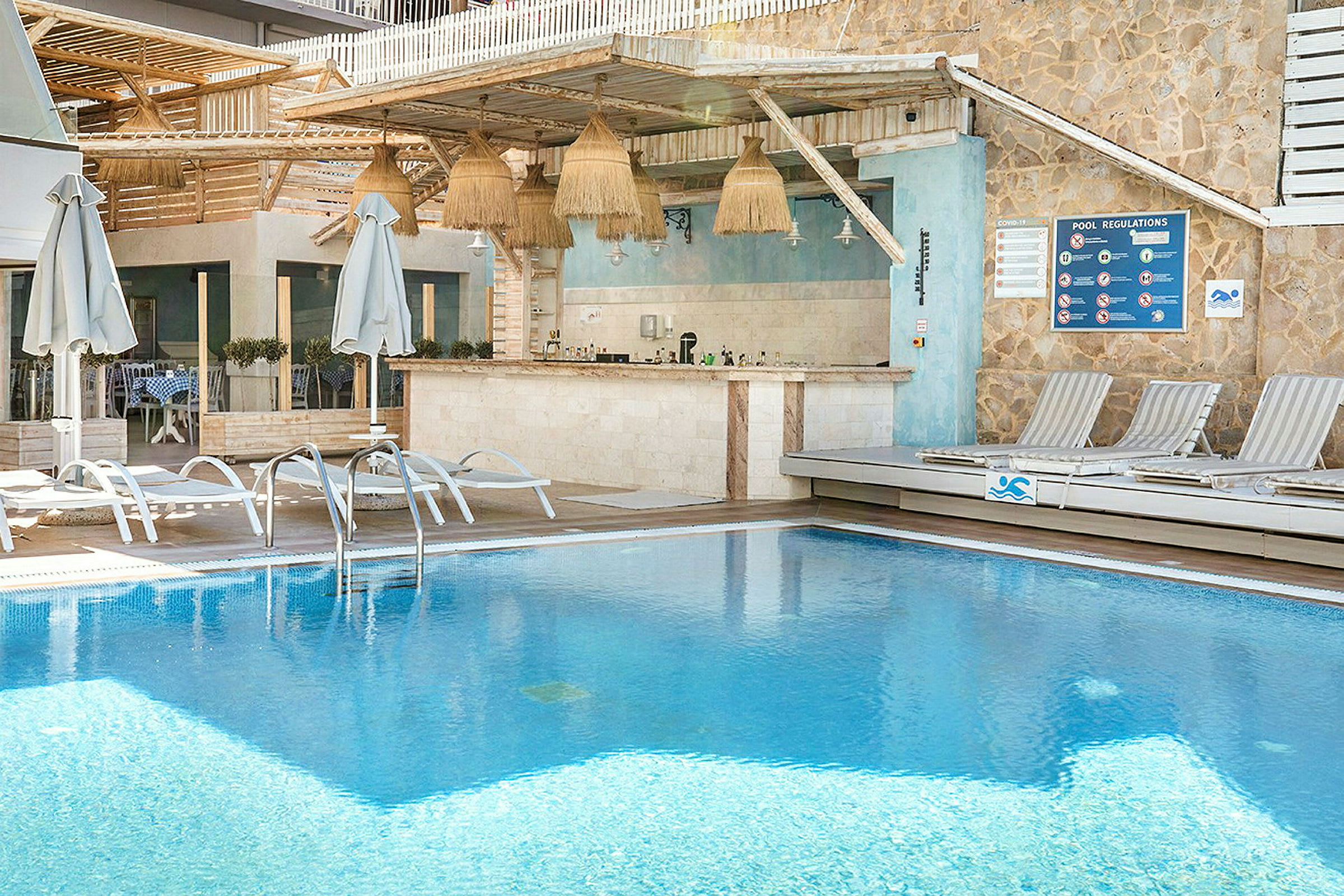 Udendørs pool med liggestole og en bar i baggrunden. (AI-genereret tekst)
