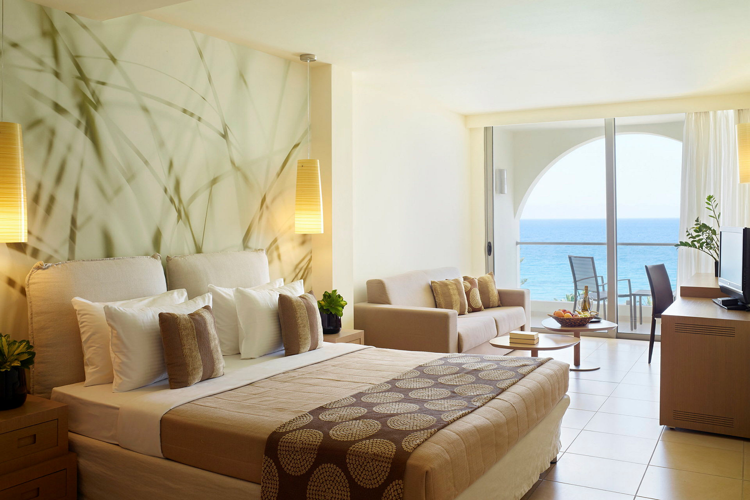 Hotelværelse med havudsigt og moderne indretning, herunder seng, sofa og balkon. (AI-genereret tekst)