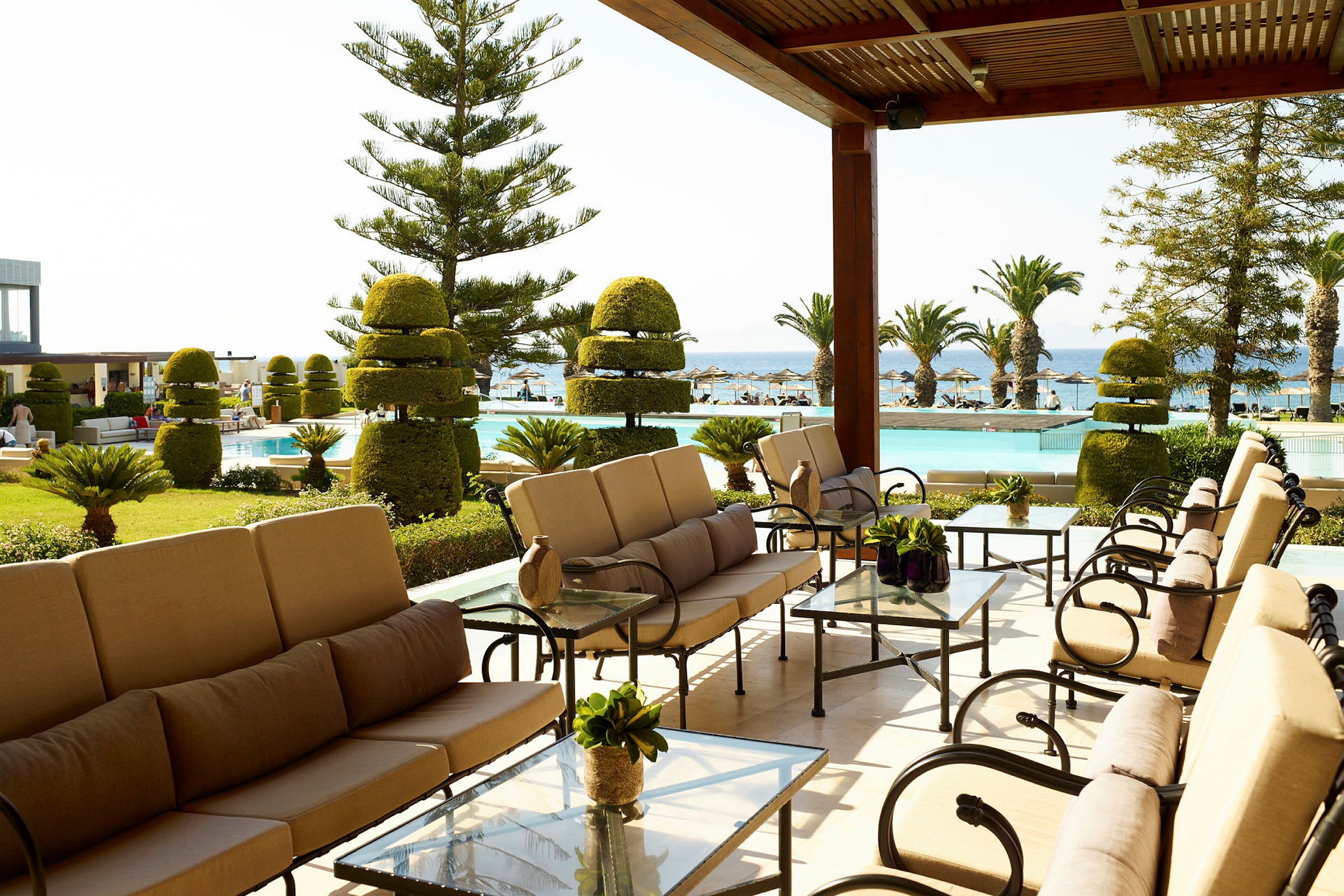 Udendørsområde med sofaer og borde nær en pool og have, der vender ud mod havet. (AI-genereret tekst)