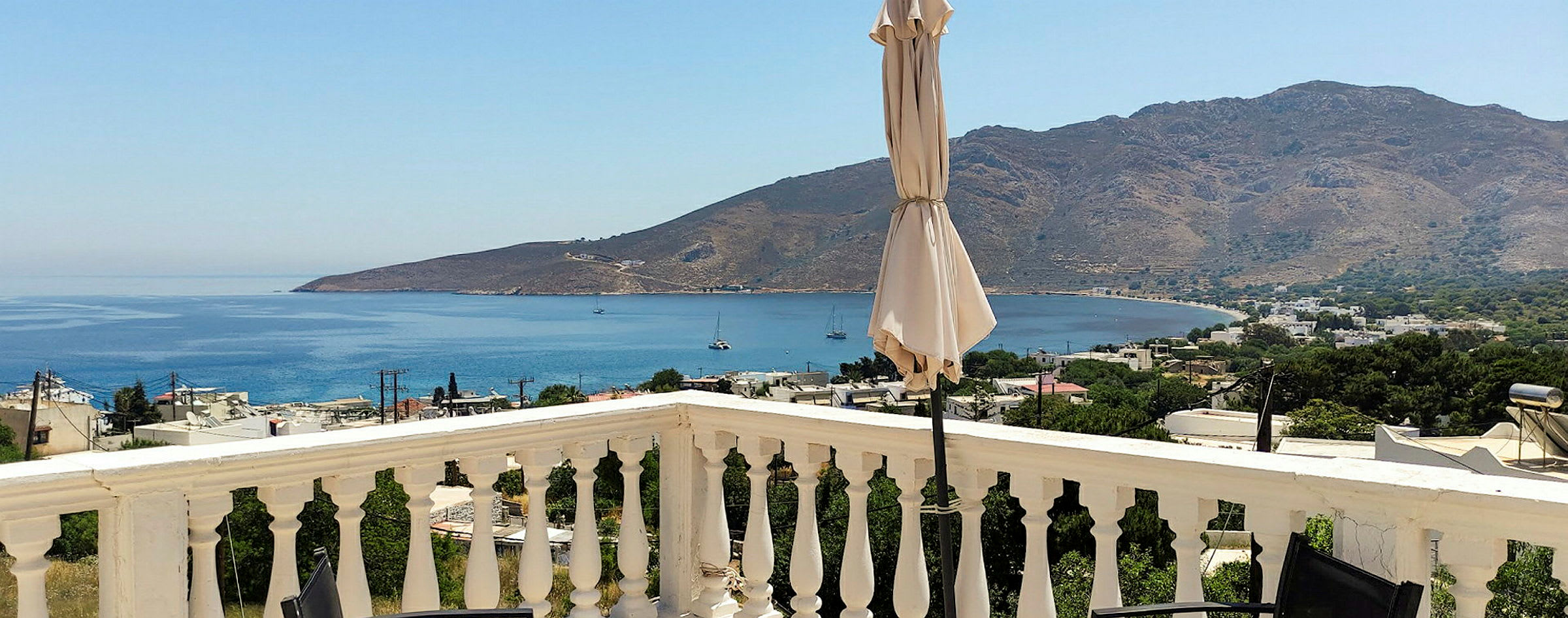 En udsigt fra en terrasse med rækværk, en parasol og havet og bjerge i baggrunden. (AI-genereret tekst)