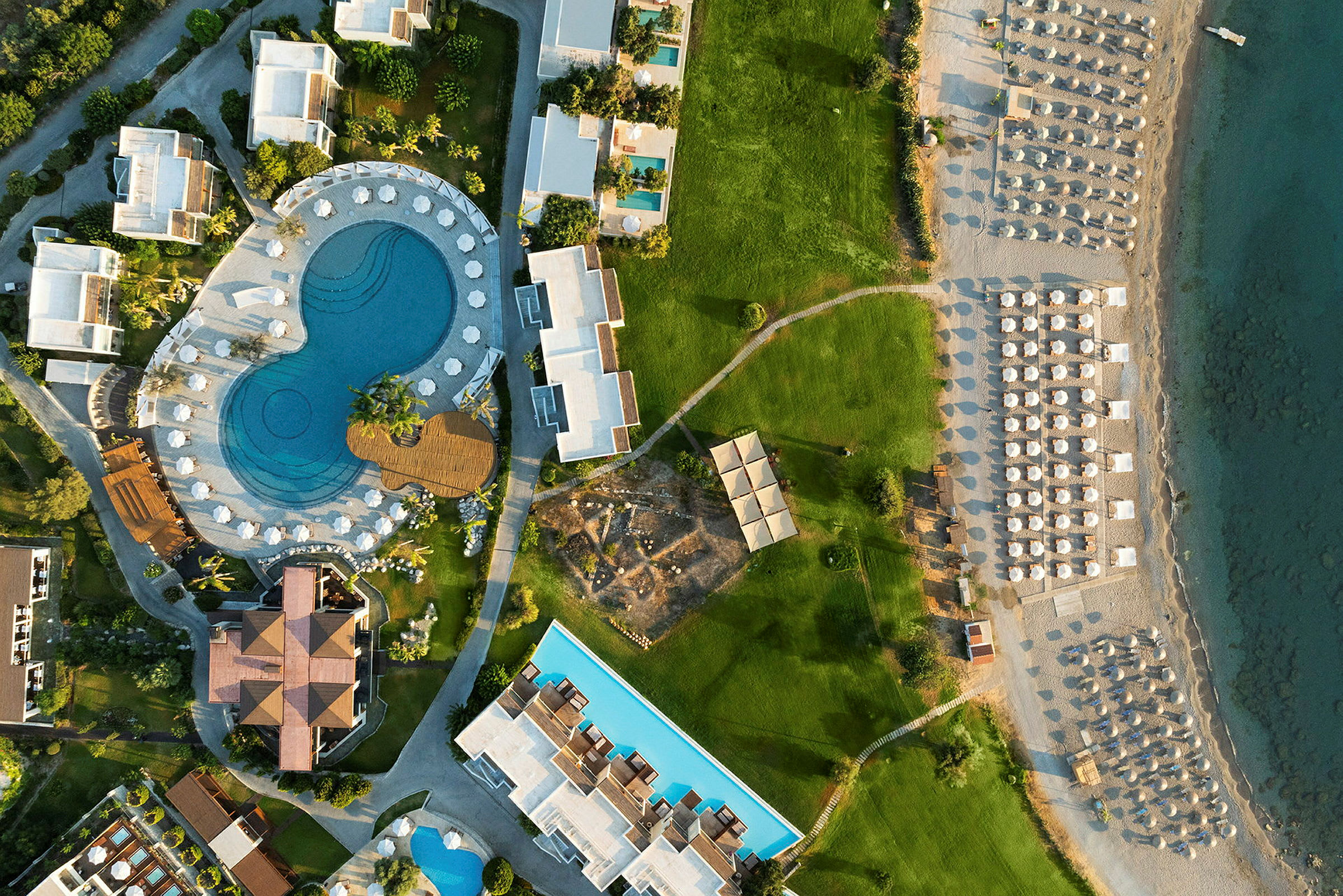 Luftfoto af et feriested med swimmingpool, grønne områder og strand med parasoller. (AI-genereret tekst)