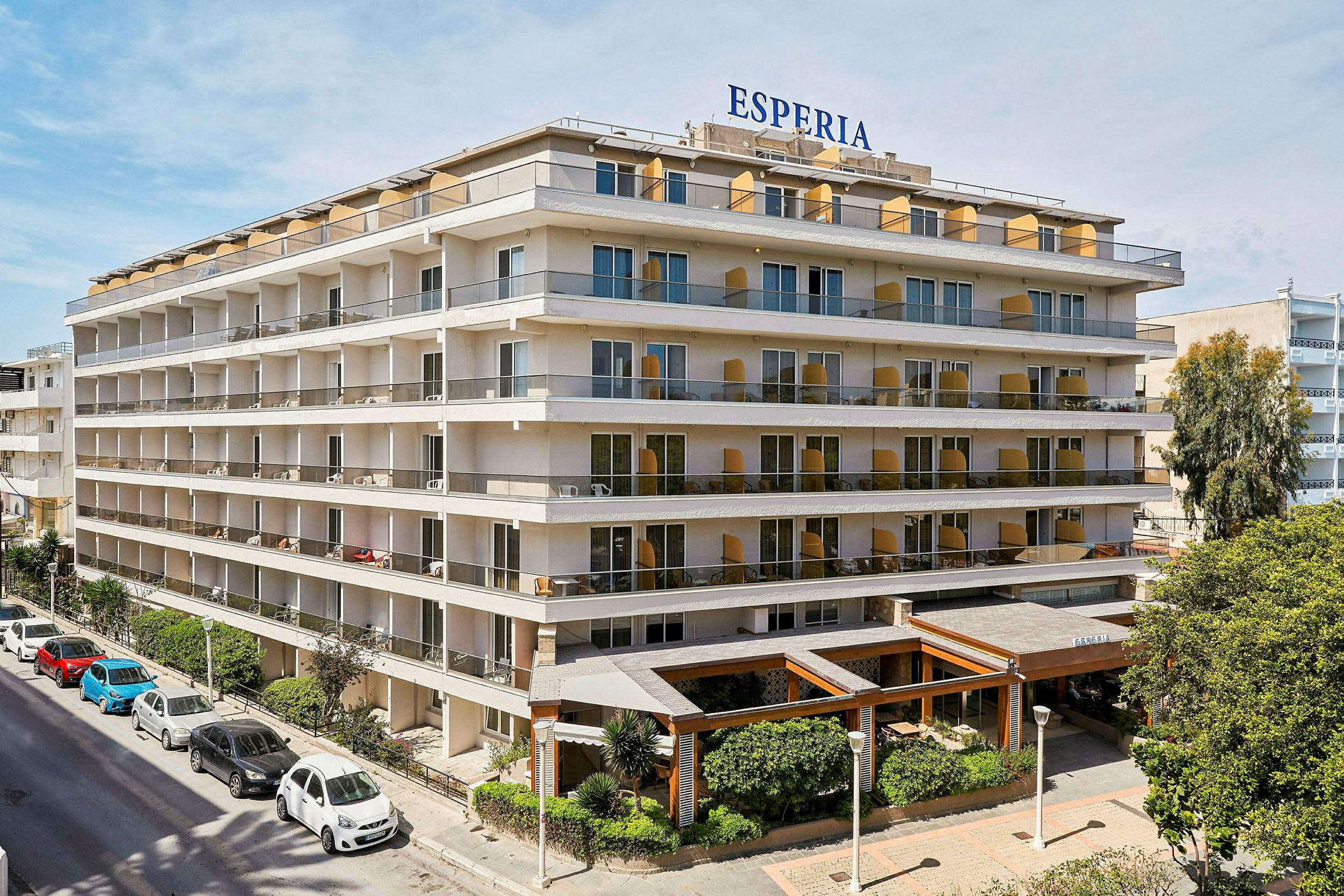 Hotel Esperia, en fleretagers bygning med store altaner og grøn beplantning ved indgangen. (AI-genereret tekst)
