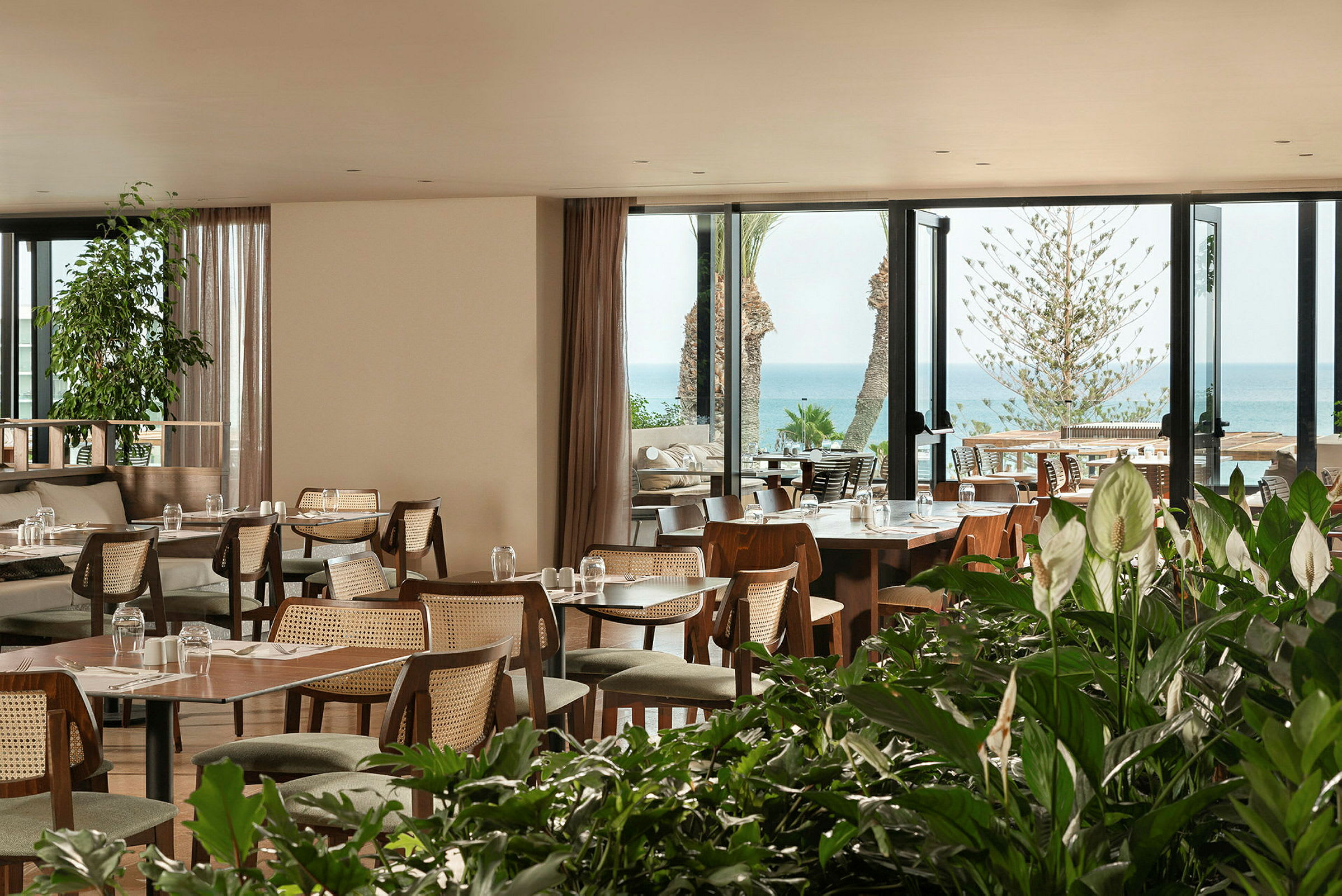 En restaurant med udsigt over havet og omgivet af grønne planter. (AI-genereret tekst)