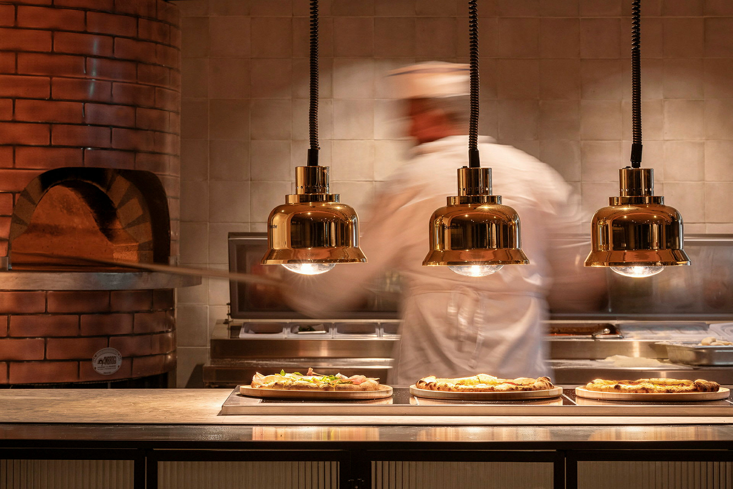 En pizzabager arbejder ved en ovn, hvor tre færdige pizzaer ligger på serveringsbordet. (AI-genereret tekst)