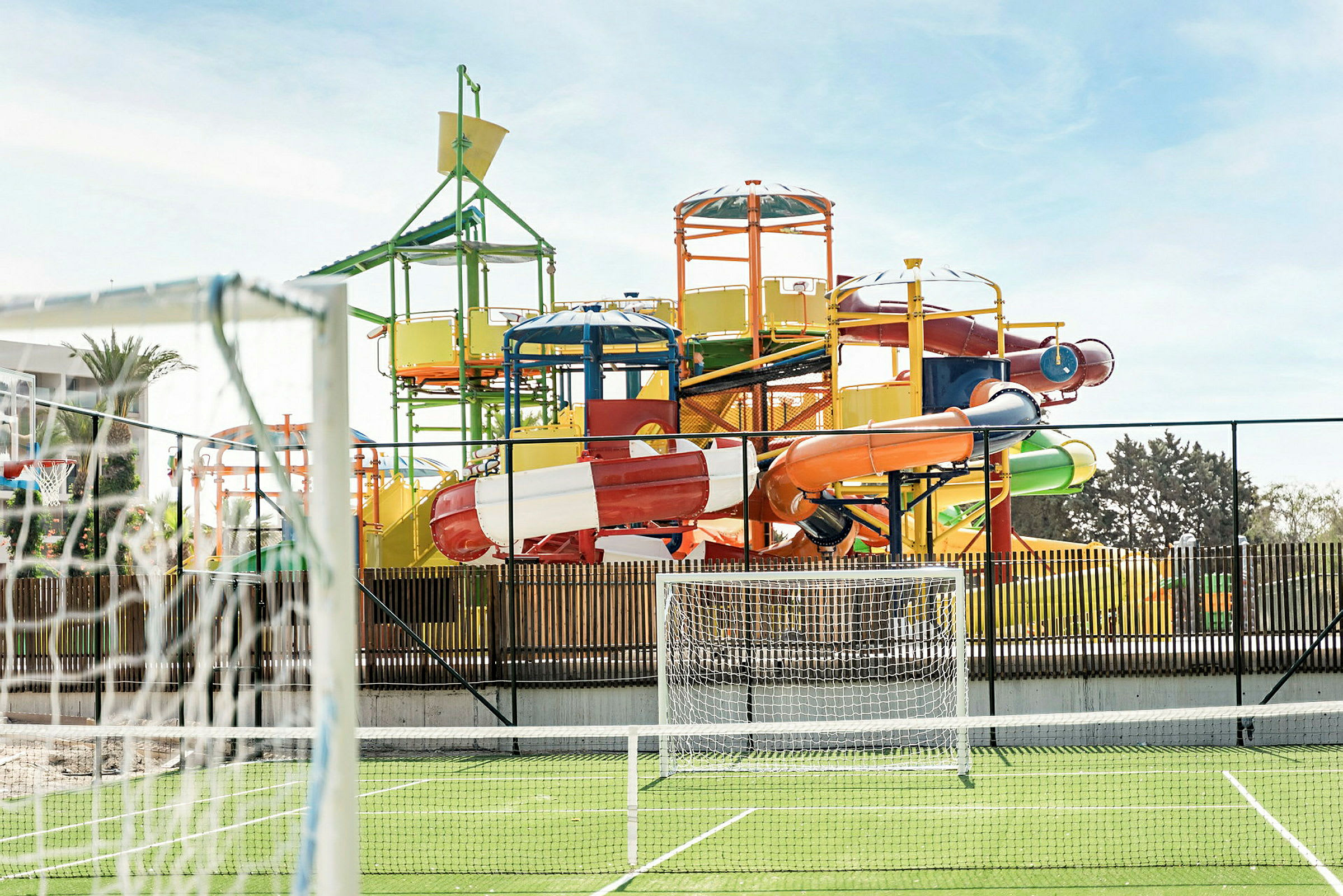 En farverig vandpark med flere vandrutsjebaner og et fodboldmål i forgrunden. (AI-genereret tekst)
