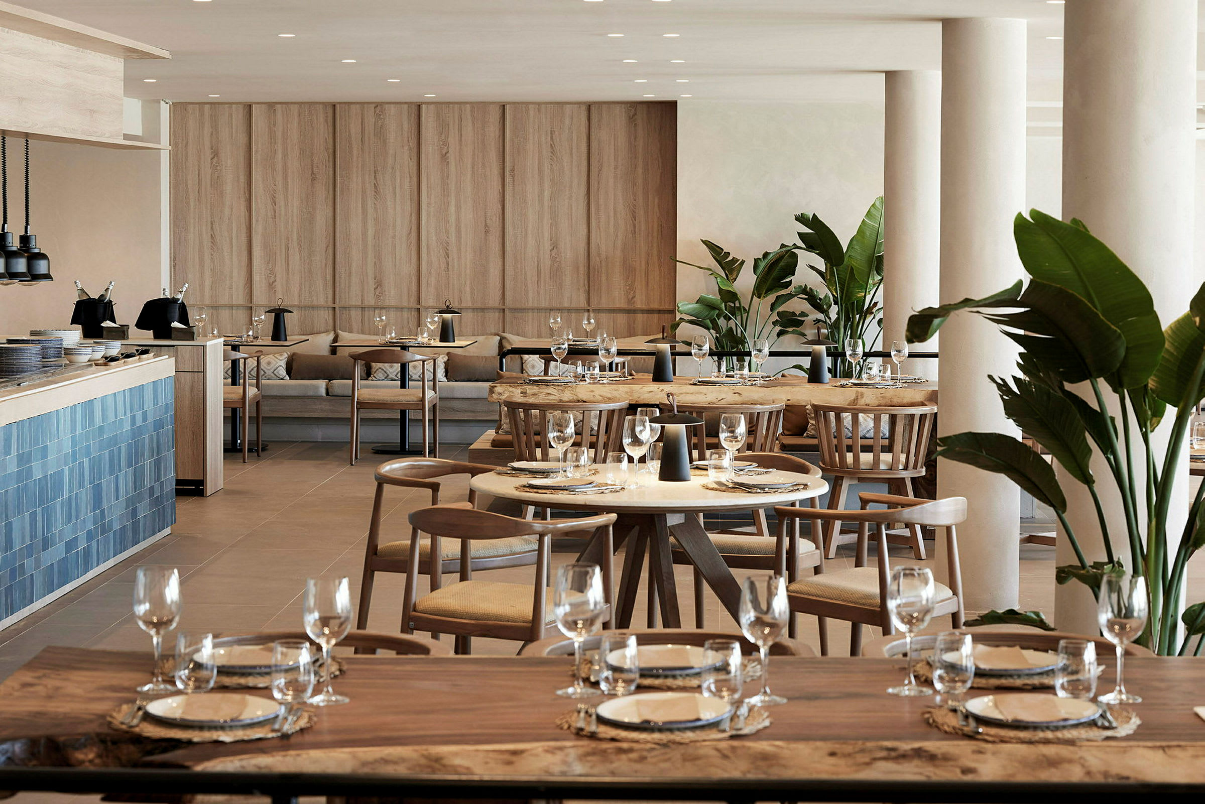 En moderne restaurant med træborde, stole og dekorative grønne planter. (AI-genereret tekst)