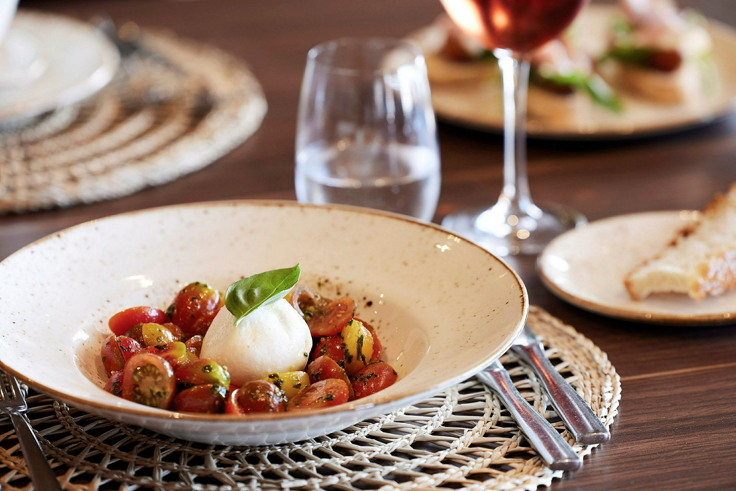 En tallerken med mozzarella og tomatsalat og et glas vand på en bord. (AI-genereret tekst)