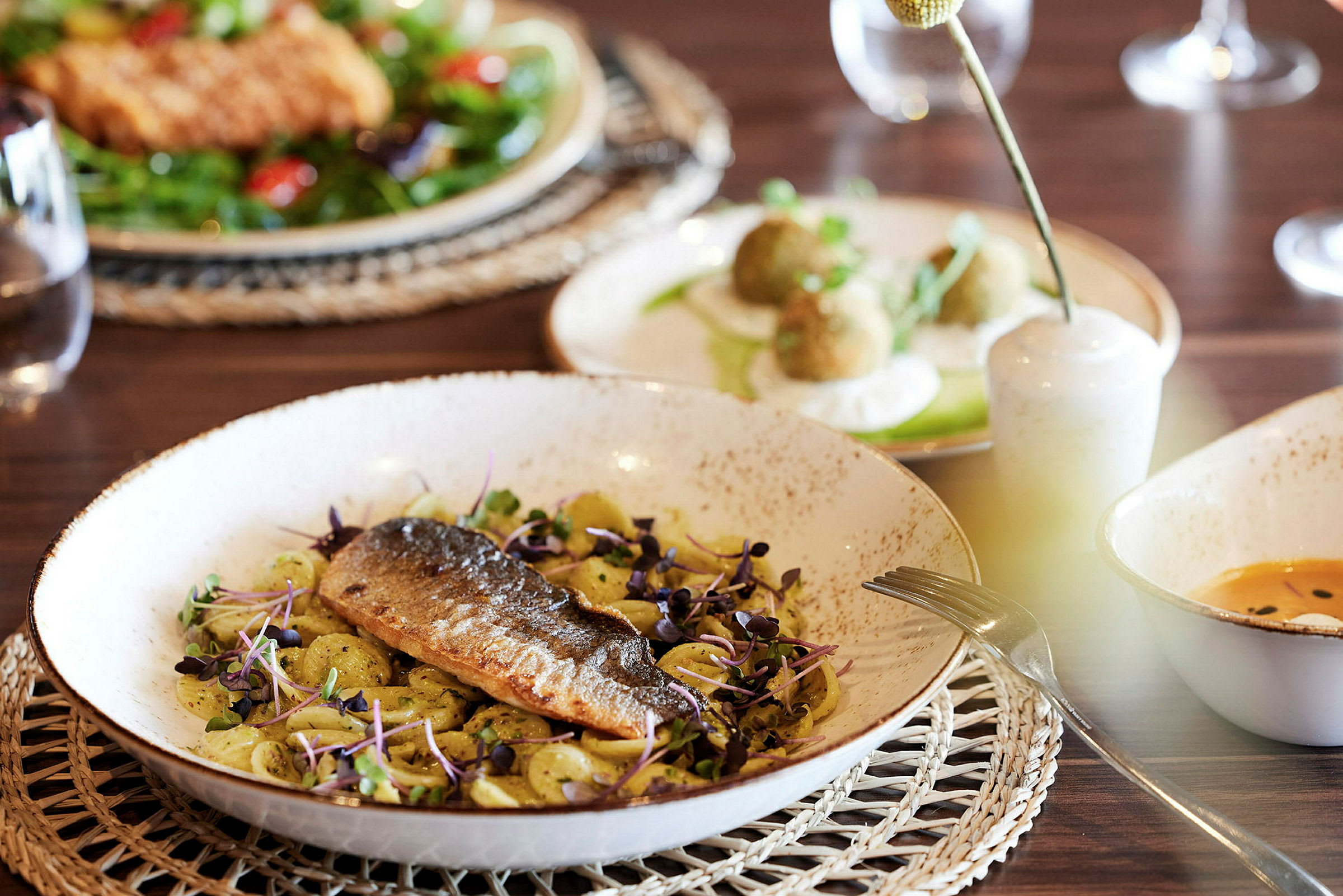 En tallerken med fisk og pasta, omgivet af andre retter på et bord. (AI-genereret tekst)