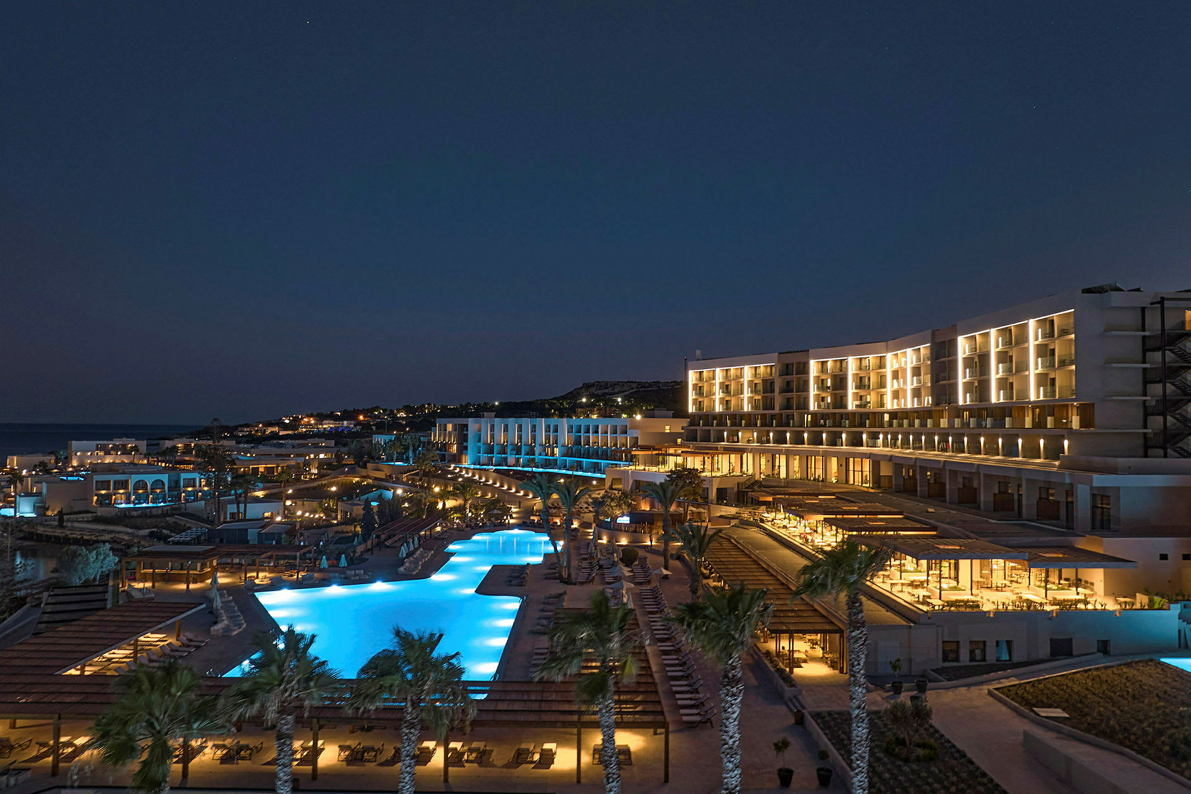Natudsigt af et oplyst hotel med poolområde og palmer. (AI-genereret tekst)