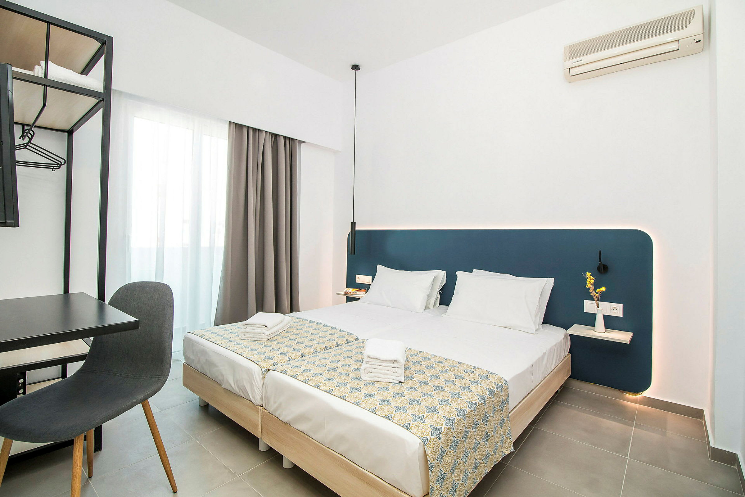 Moderne hotelværelse med to opredte enkeltsenge, skrivebord og stol samt vægmonteret aircondition. (AI-genereret tekst)