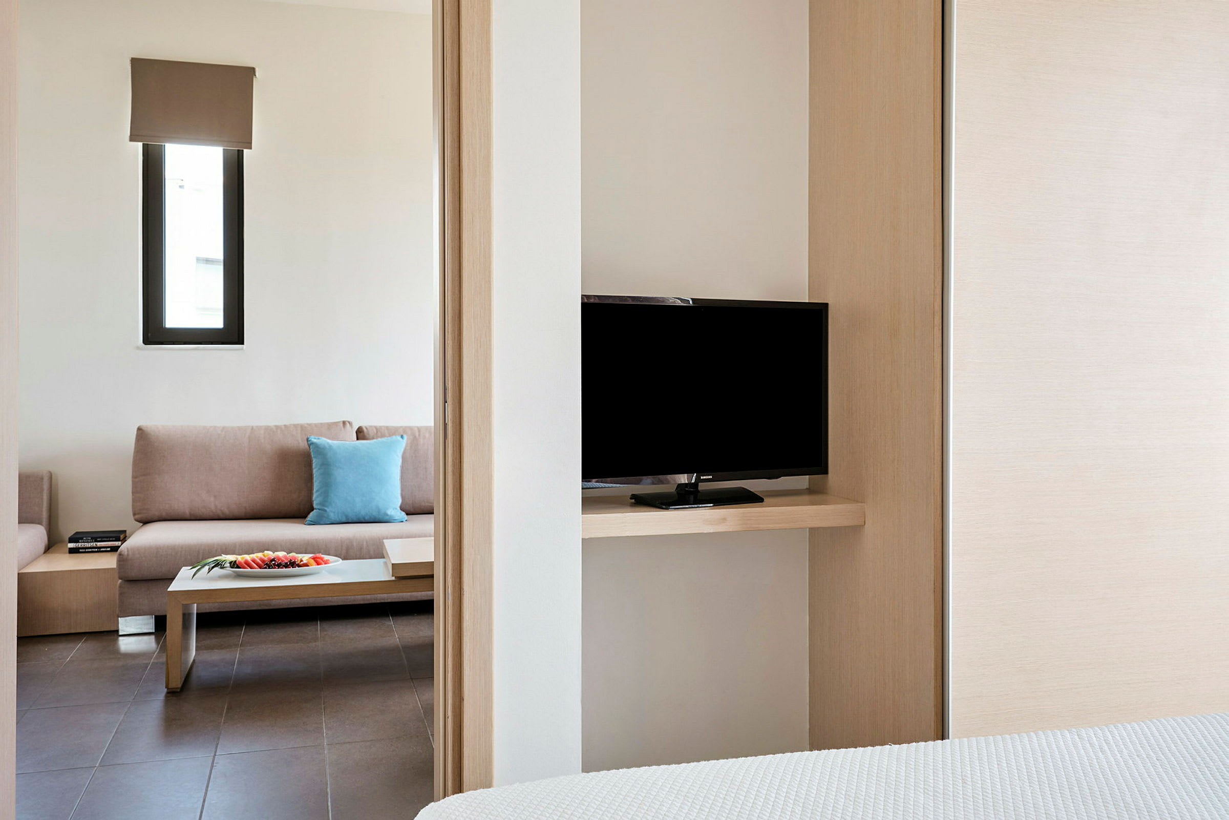 Et hotelværelse med en sofa, et sidebord og et tv synligt fra soveværelset. (AI-genereret tekst)