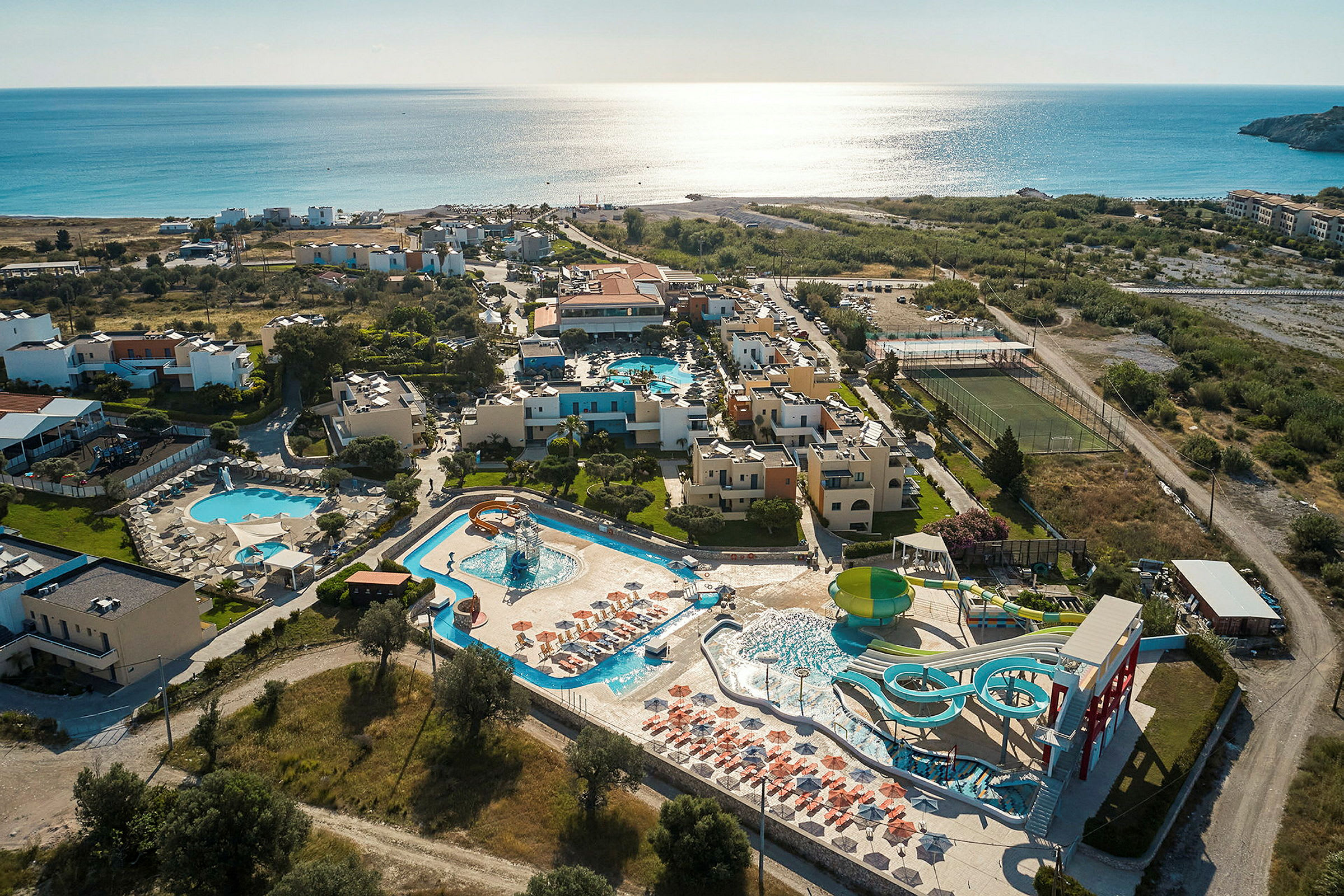 Luftfoto af en resort ved havet med poolområder og vandrutsjebaner. (AI-genereret tekst)
