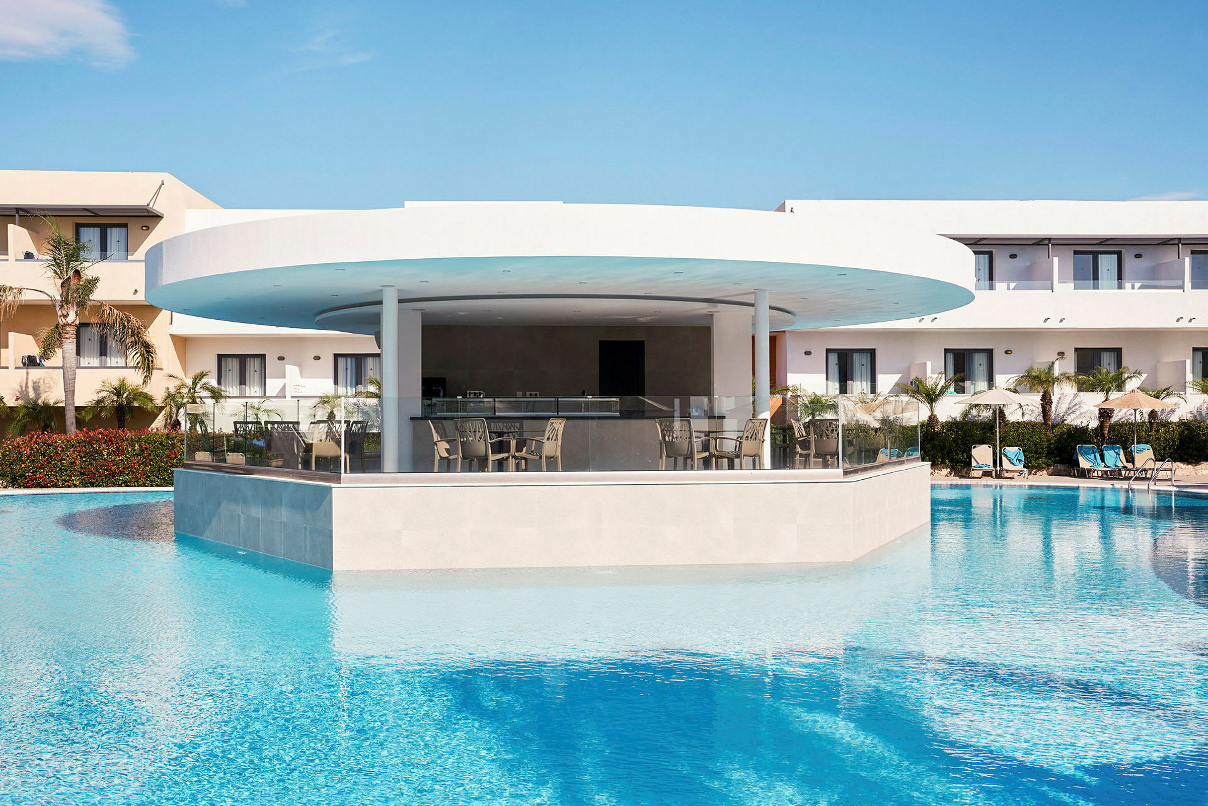 En moderne hotelbar omgivet af en pool med klart vand og liggestole i baggrunden. (AI-genereret tekst)