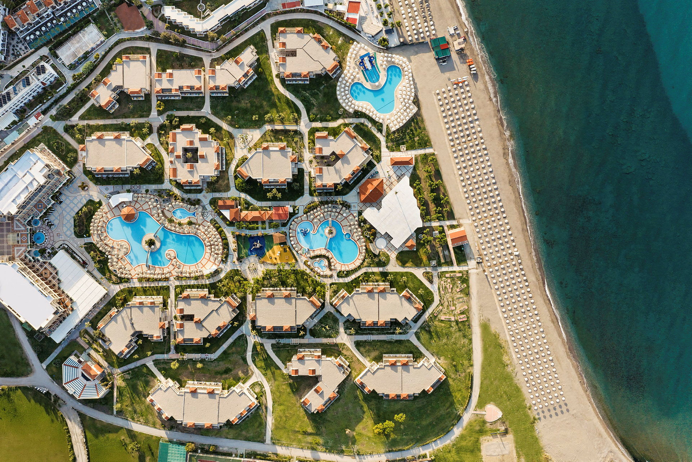 Luftfoto af et feriested med pools, bygninger og nærliggende strand. (AI-genereret tekst)