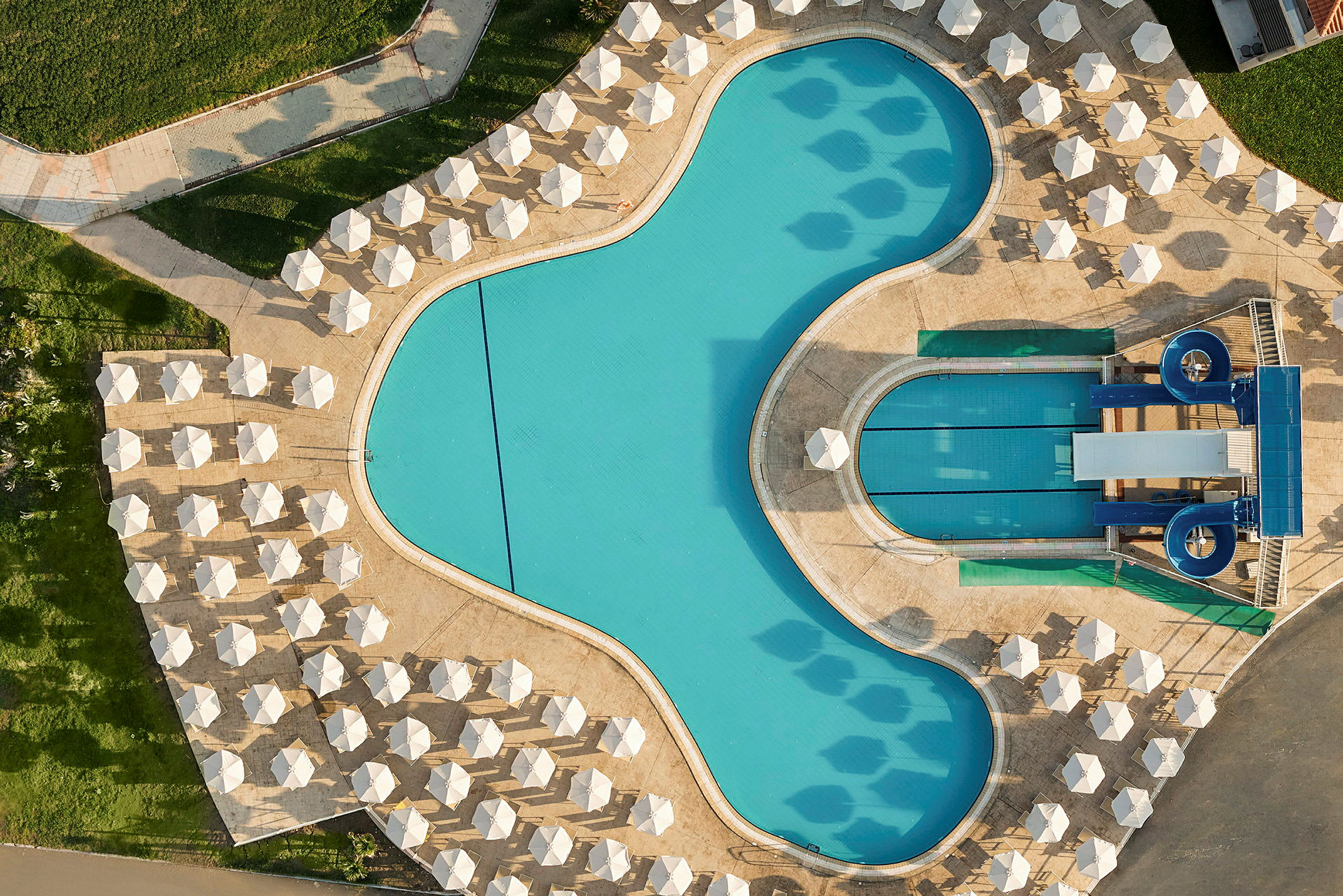 Et luftfoto af en udendørs pool med parasoller og liggestole omkring. (AI-genereret tekst)
