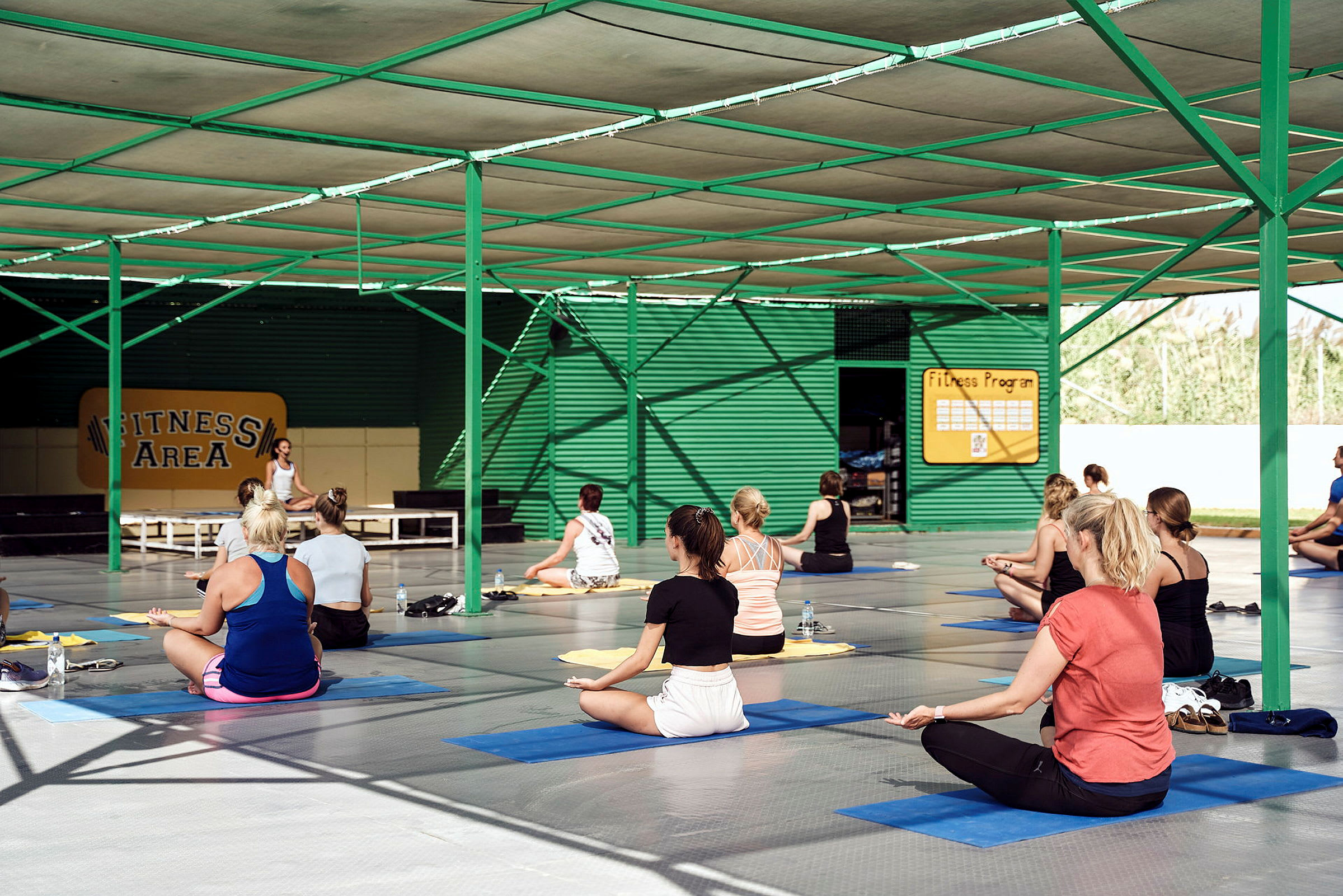 Personer udfører træning på yogamåtter i et overdækket fitnessområde. (AI-genereret tekst)
