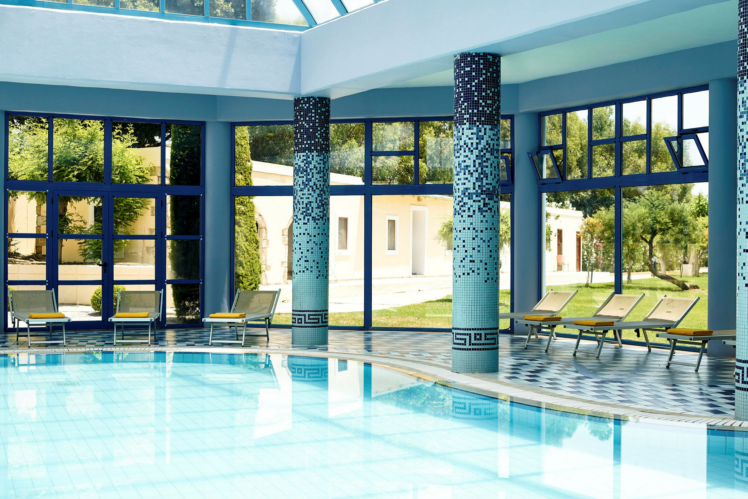 Indendørs pool med blå mosaik og liggestole ved vinduer. (AI-genereret tekst)