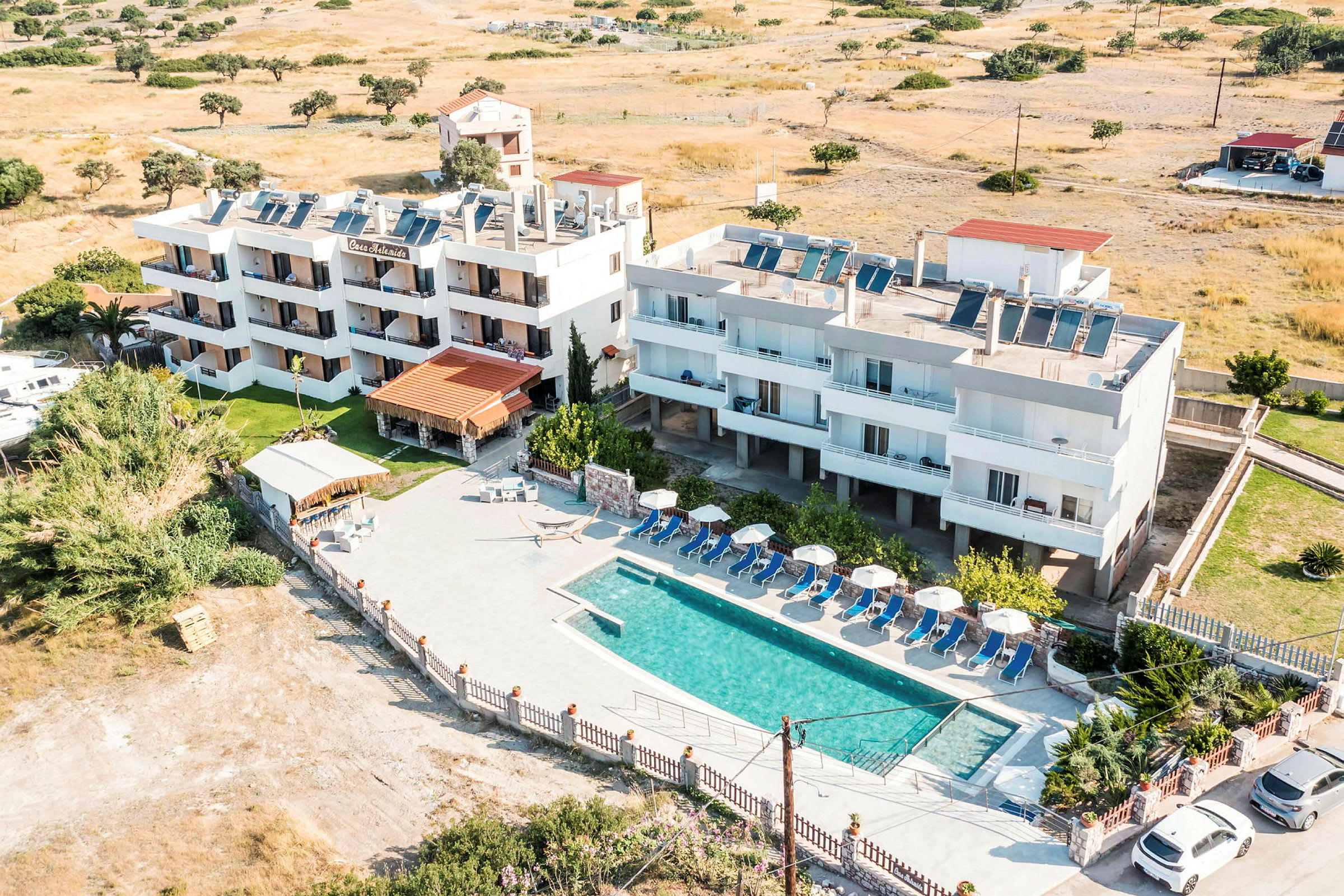 Billede af et hotel med pool og liggestole samt omkringliggende landskab. (AI-genereret tekst)