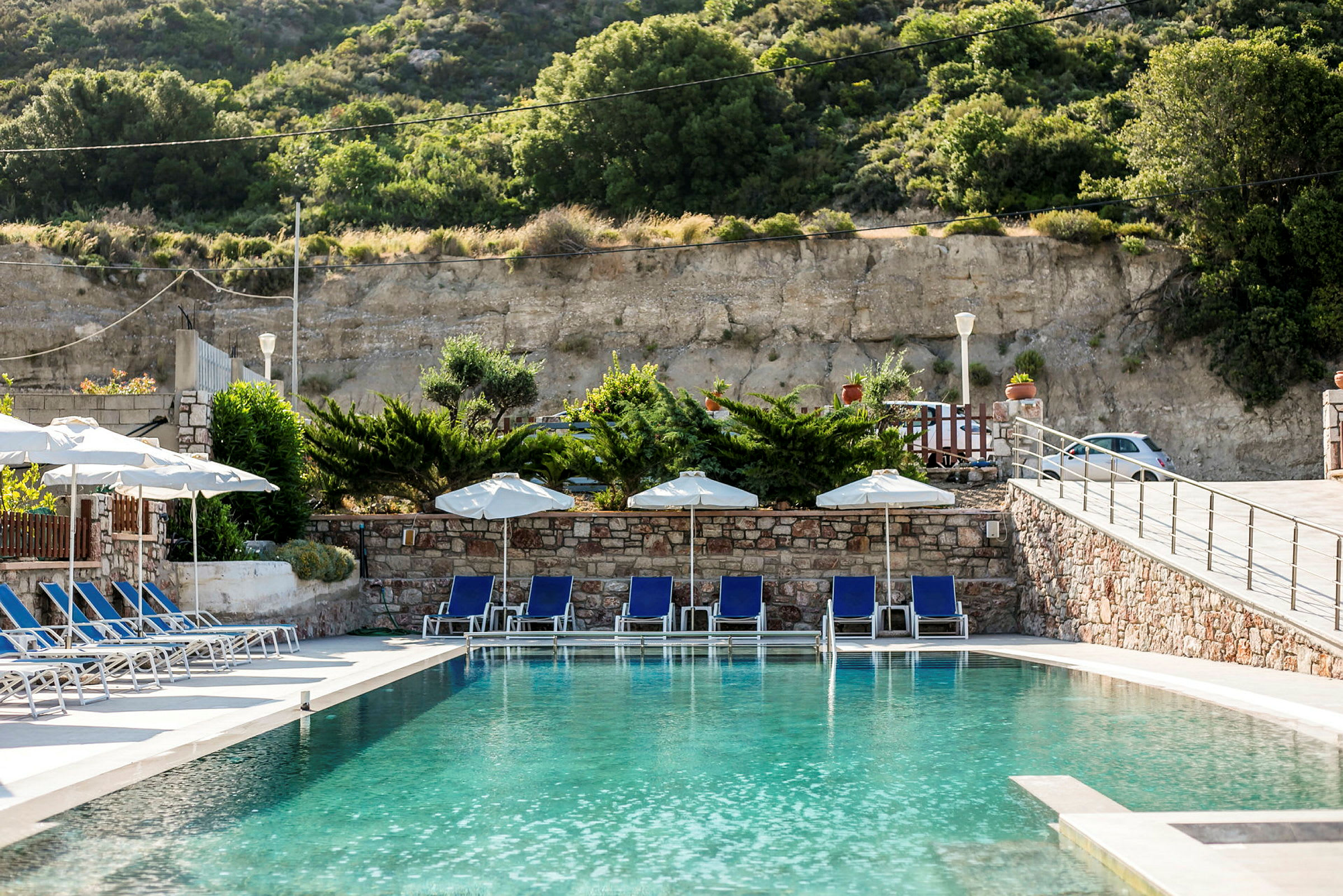Pool med liggestole, parasoller og grønt i baggrunden. (AI-genereret tekst)