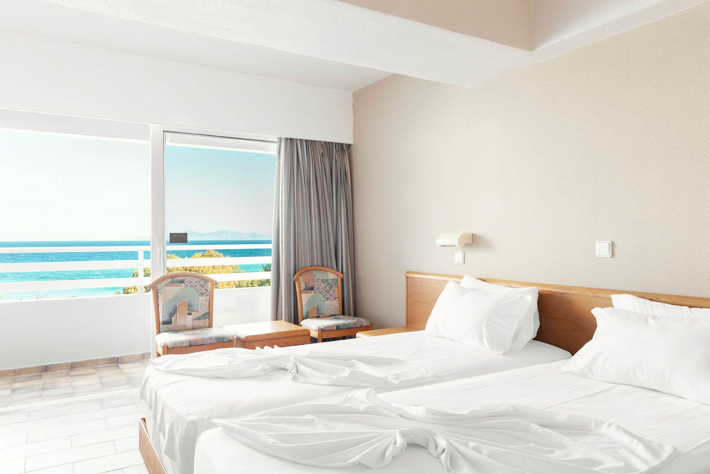 Et hotelværelse med to enkeltsenge og en balkon med udsigt over havet. (AI-genereret tekst)